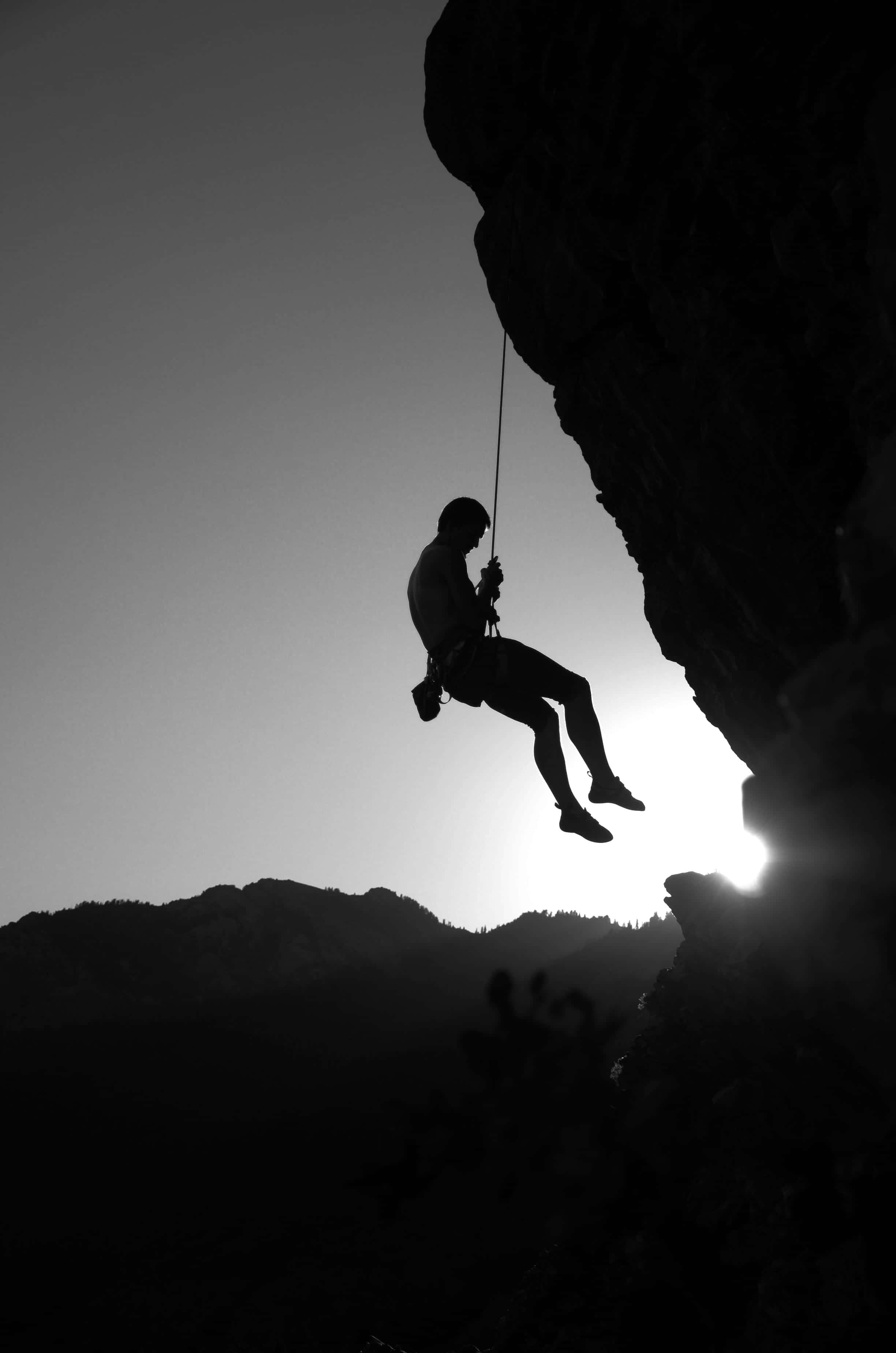 Climbing 桌布 壁紙 — 一名攀岩者的剪影在日落時分沿懸崖面下降，背光投射出戲劇性的陰影。