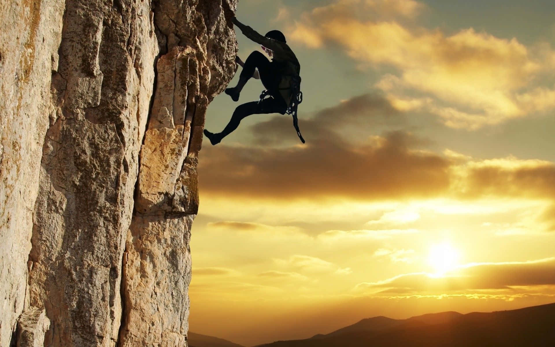 Rock Climbing 桌布 壁紙 — 一名攀岩者的剪影在金色日落天空和遠處山脈的映襯下攀登崎嶇的懸崖面。