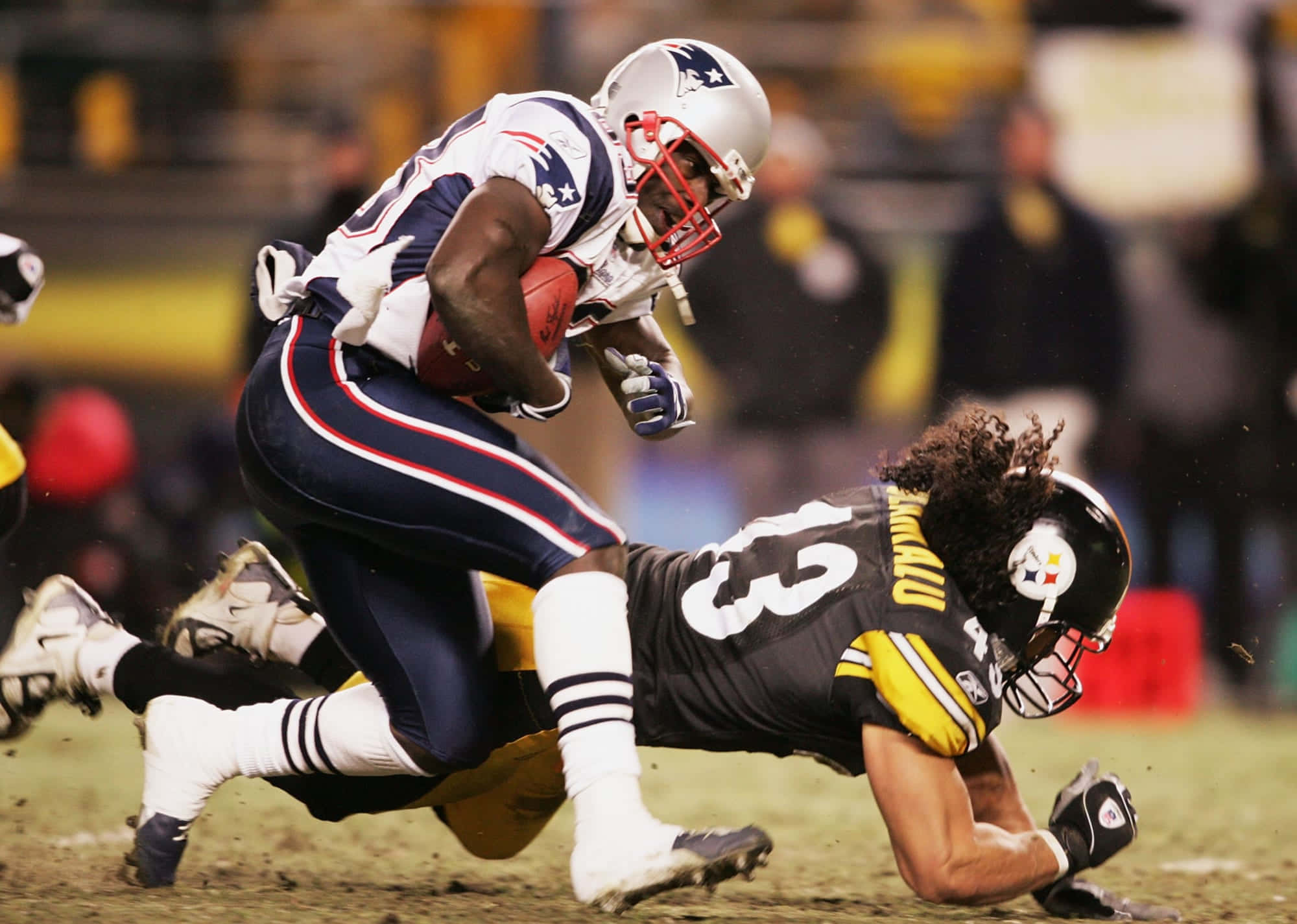 Troy Polamalu 桌布 壁紙 — 一名新英格蘭愛國者球員在泥濘的球場上被匹茲堡鋼人隊防守球員擒抱時緊緊抓住足球。