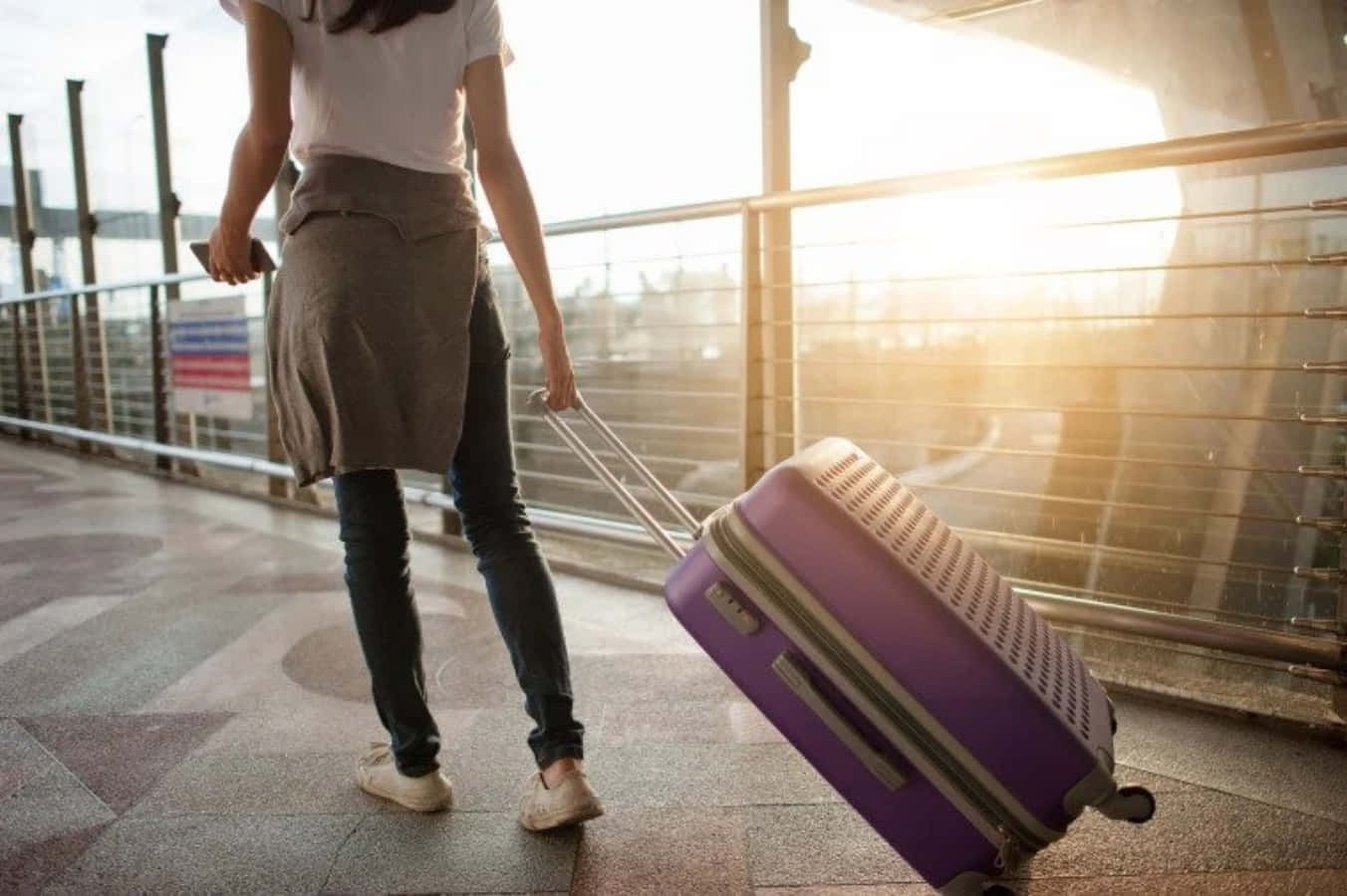 Traveling 桌布 壁紙 — 一名旅客在陽光普照的現代化航廈中拉著紫色行李箱，背景帶有溫暖的背光。