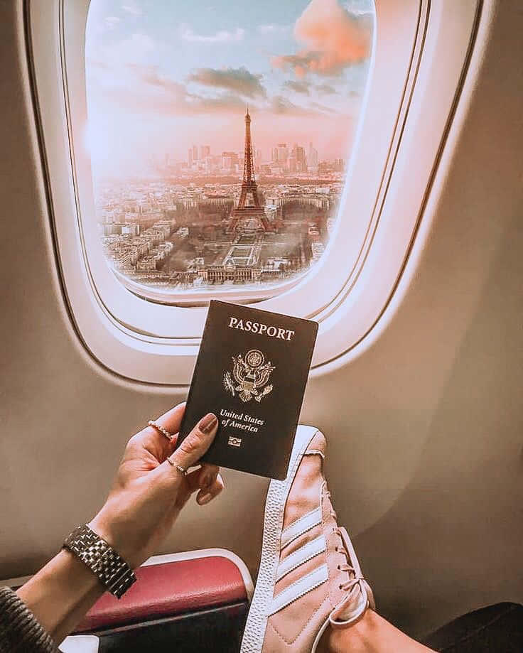 Passport 桌布 壁紙 — 一名旅客在飛機窗前手持美國護照，俯瞰巴黎，背景是日落時分的艾菲爾鐵塔。