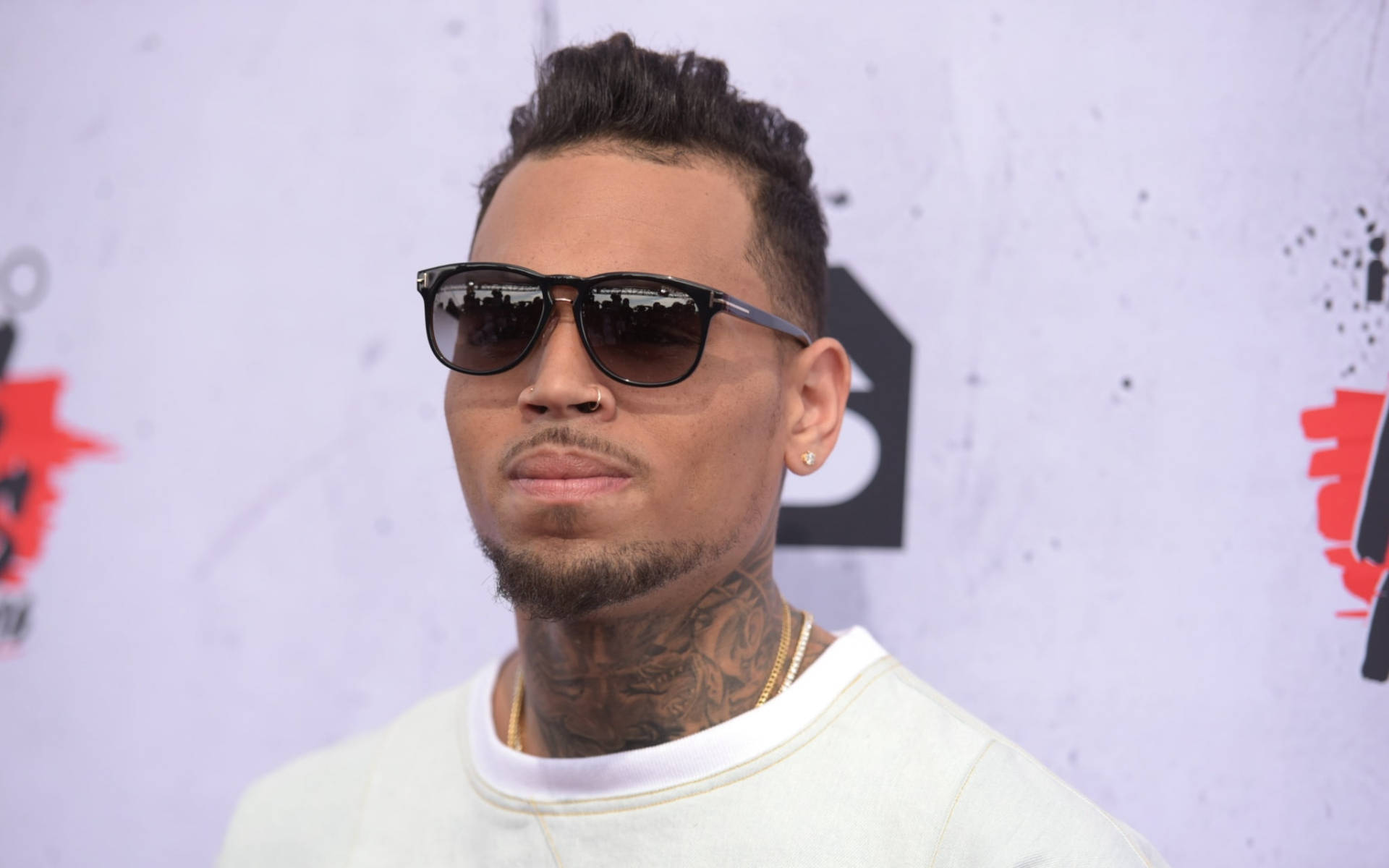 Chris Brown 桌布 壁紙 — 一名有刺青和戴太陽眼鏡的男子在品牌背景前自信地擺姿勢，出席紅地毯活動。