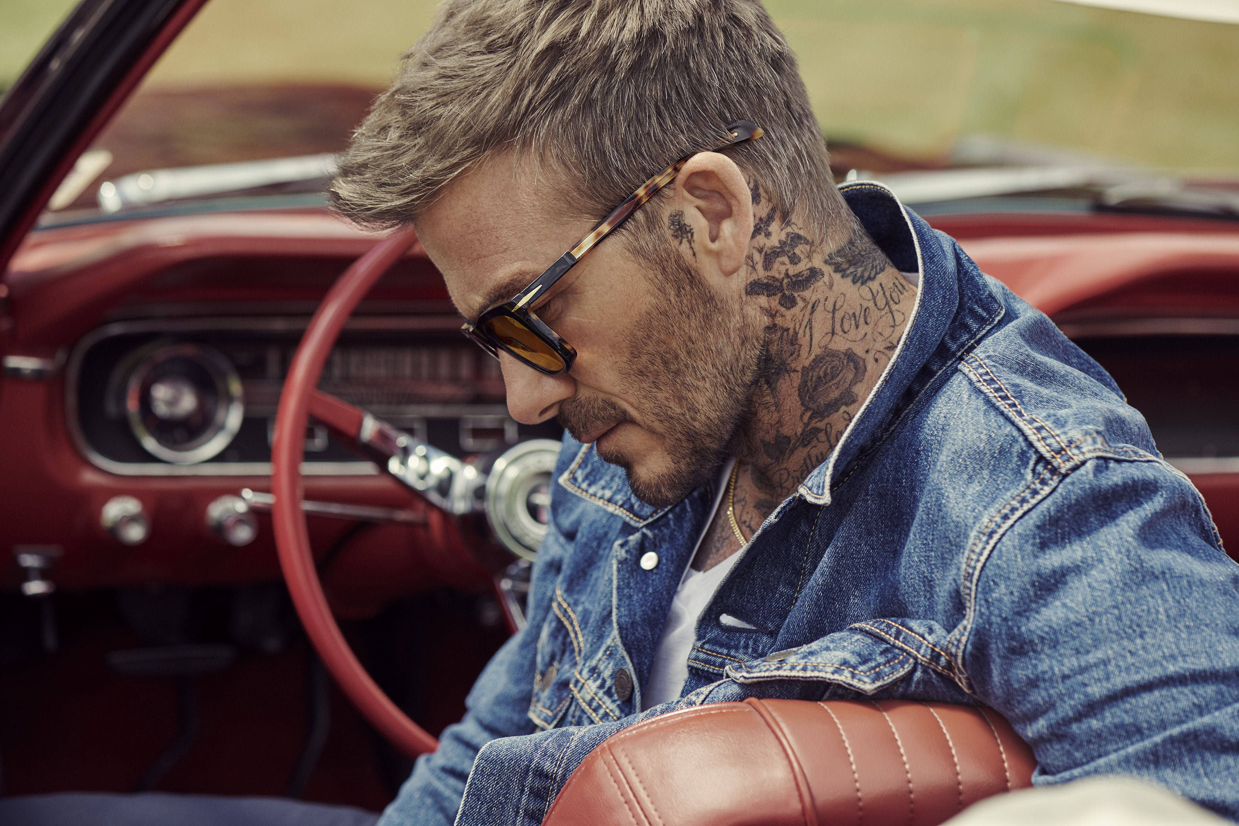 David Beckham 桌布 壁紙 — 一名有刺青和戴太陽眼鏡的男子坐在一輛復古紅色敞篷車上，若有所思地向下看。