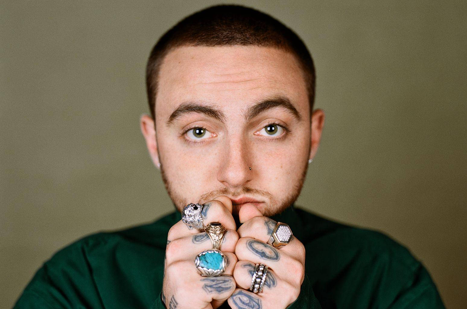Mac Miller 桌布 壁紙 — 一名有刺青和戴著多個戒指的男子，在柔和的綠色背景下凝視著鏡頭。