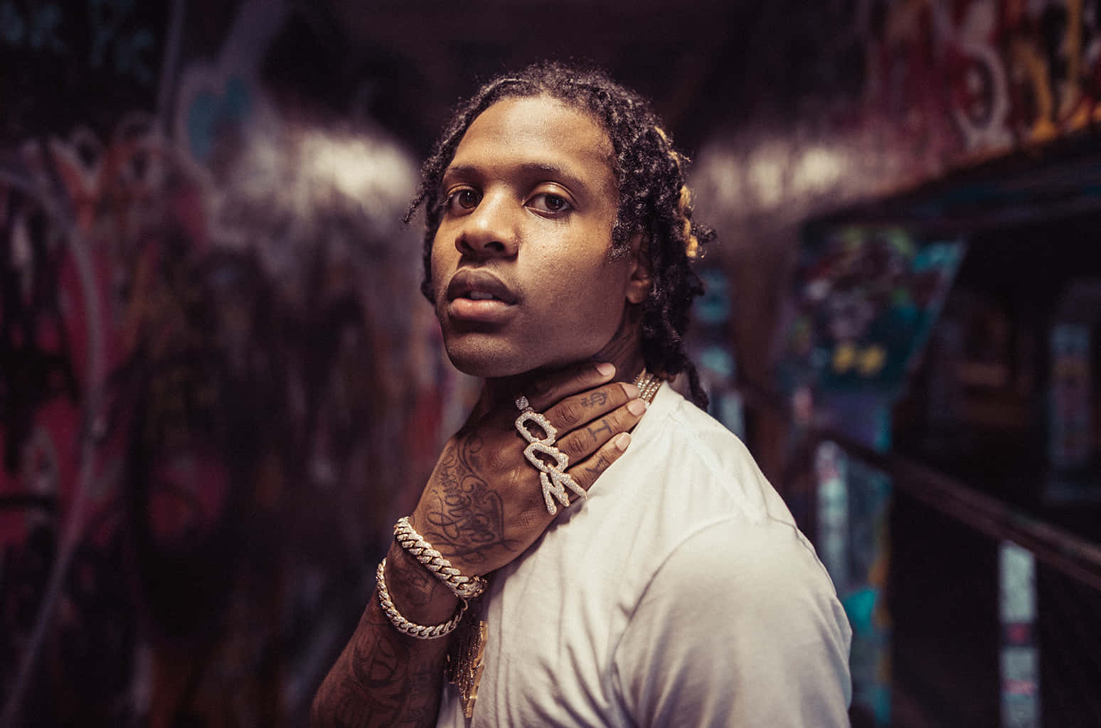 Lil Durk 桌布 壁紙 — 一名有刺青和戴金鍊的男子在昏暗的城市環境中，自信地以塗鴉牆為背景擺姿勢。