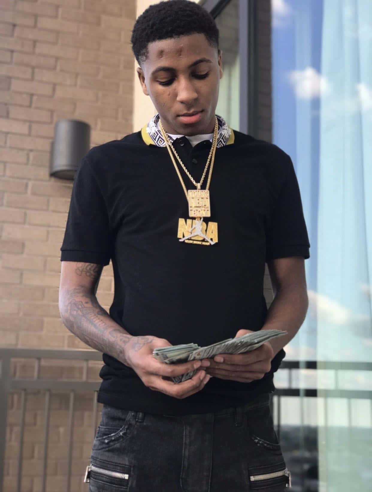 Youngboy 桌布 壁紙 — 一名有刺青和戴金項鍊的年輕男子站在磚造建築外數現金。