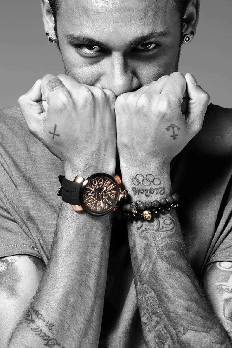 Tattoo 桌布 壁紙 — 一名有刺青和耳環的男子，戴著手錶和珠串手鍊，握緊拳頭靠近臉部，眼神銳利。