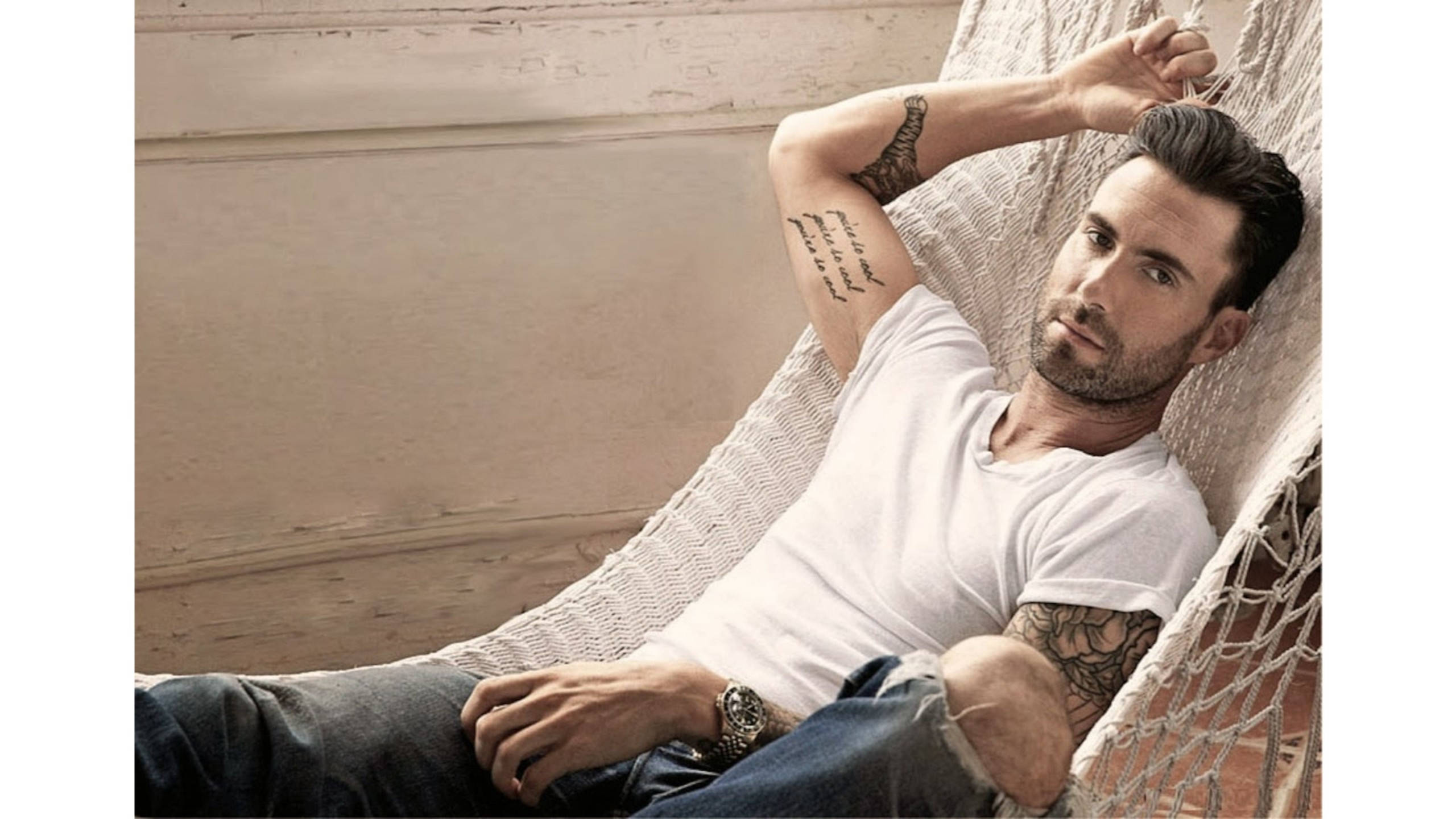 Adam Levine 桌布 壁紙 — 一名有刺青的男子在白色吊床上放鬆，背景是風化的木牆。