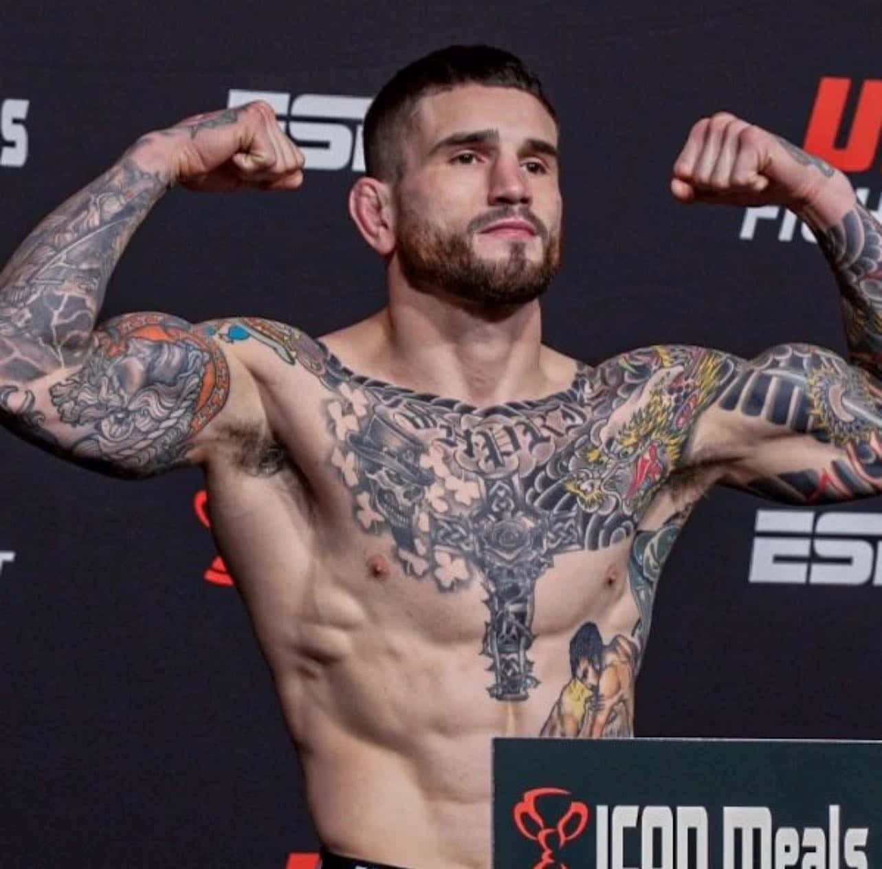 MMA 桌布 壁紙 — 一名有刺青的男性拳手在稱重活動中展示他肌肉發達的手臂，背後有ESPN和ICON Meals的品牌標誌。