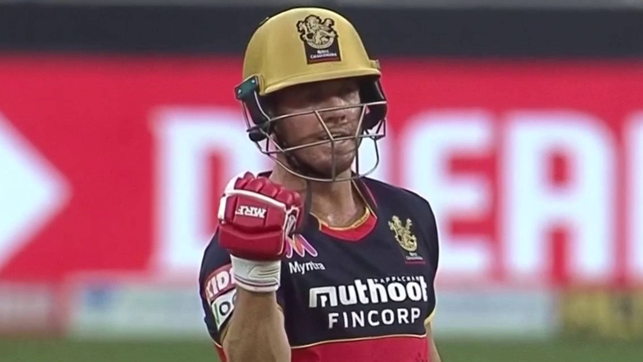 royal challengers bangalore 桌布 壁紙 — 一名板球運動員戴著金色頭盔和紅色手套，在燈光明亮的場地上高舉拳頭慶祝勝利。