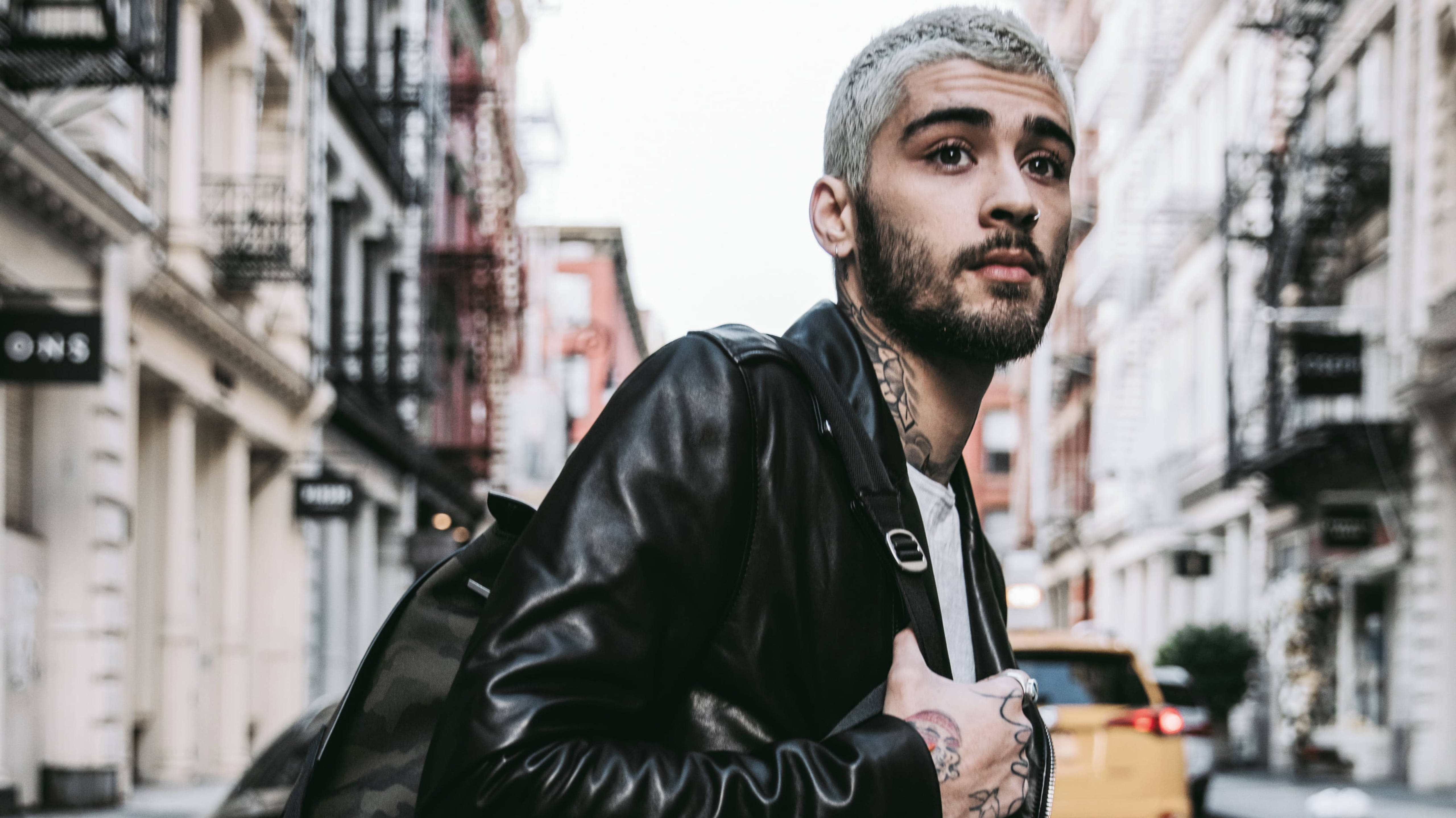 zayn 桌布 壁紙 — 一名染了淺色頭髮和刺青的年輕男子，穿著黑色皮夾克，在城市街道上凝視著。