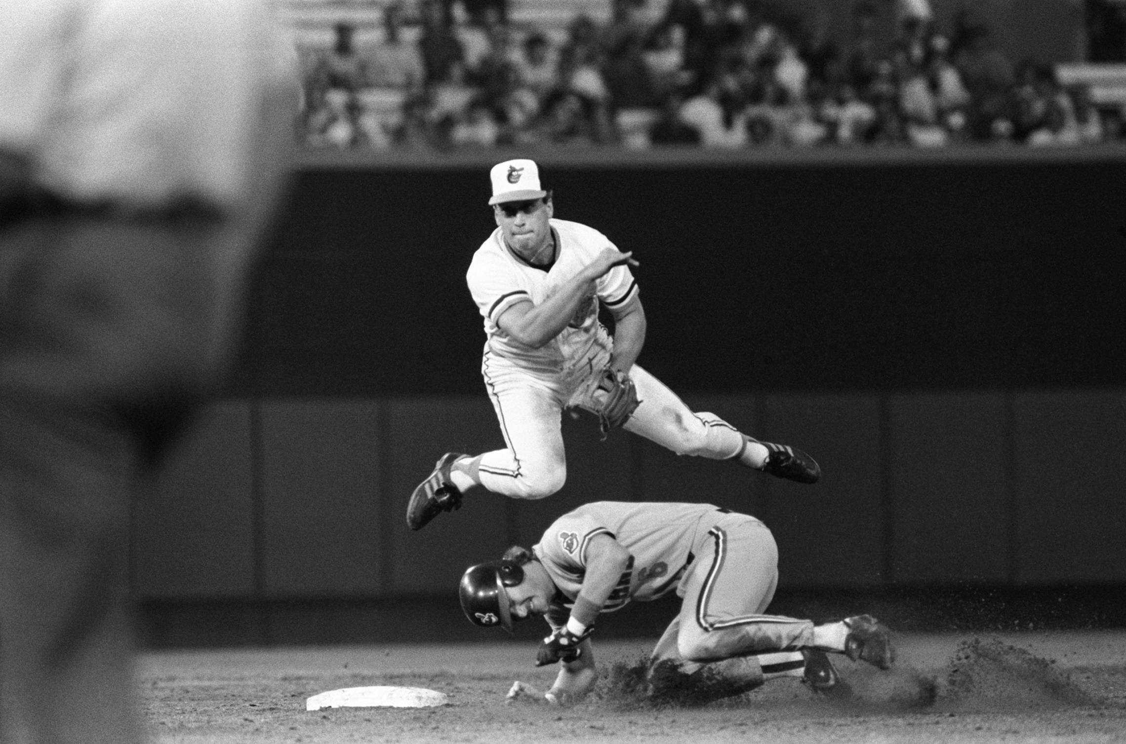 cal ripken jr 桌布 壁紙 — 一名棒球運動員在半空中跳躍，在本壘板前將滑壘的跑者觸殺出局，是一張戲劇性的黑白動作照片。
