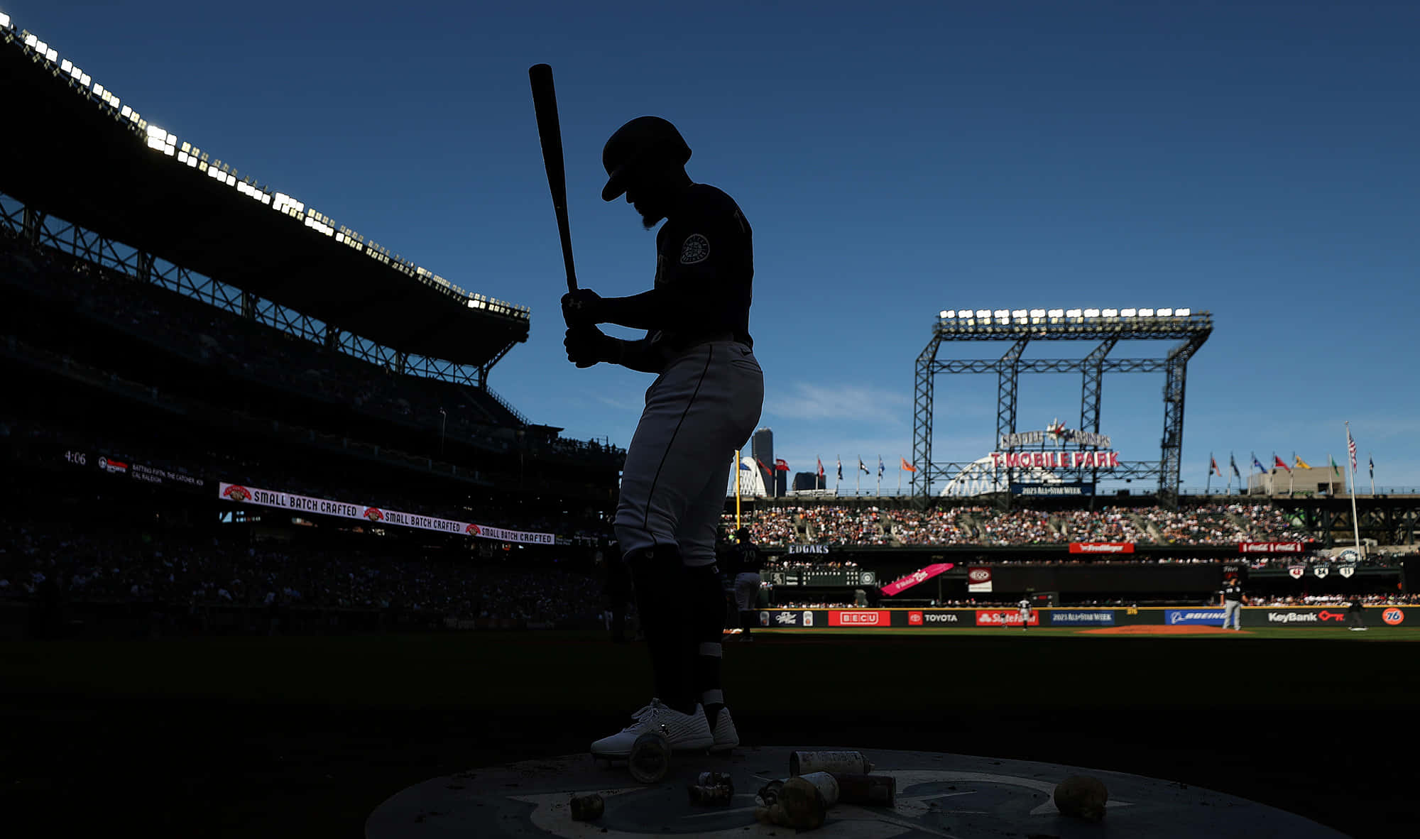 baseball bat 桌布 壁紙 — 一名棒球運動員在擠滿觀眾的球場中，以剪影姿態站在本壘板前，背景是明亮的藍天。