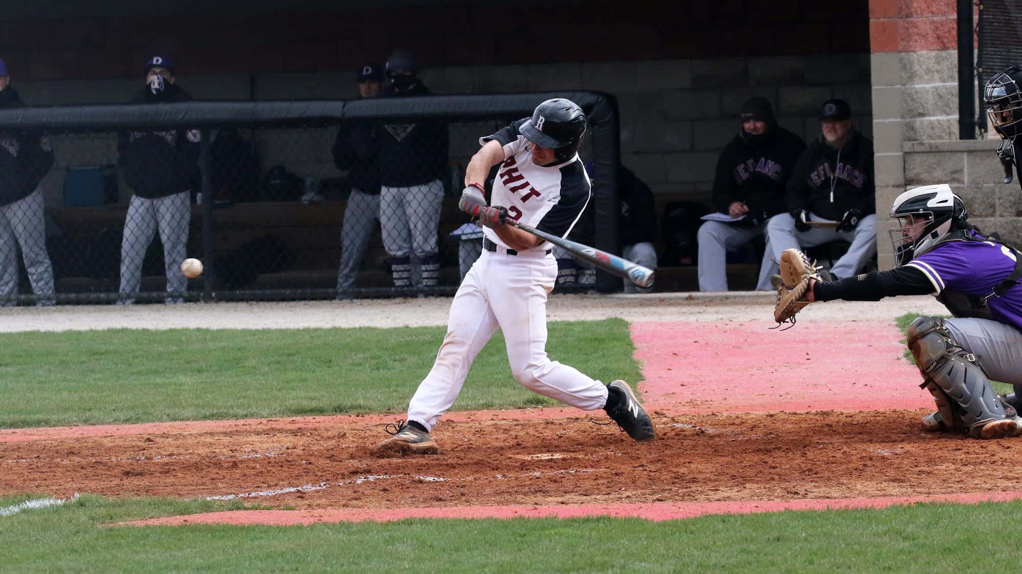 College Baseball 桌布 壁紙 — 一名棒球選手揮棒擊球，捕手蹲在本壘板後方準備接球。