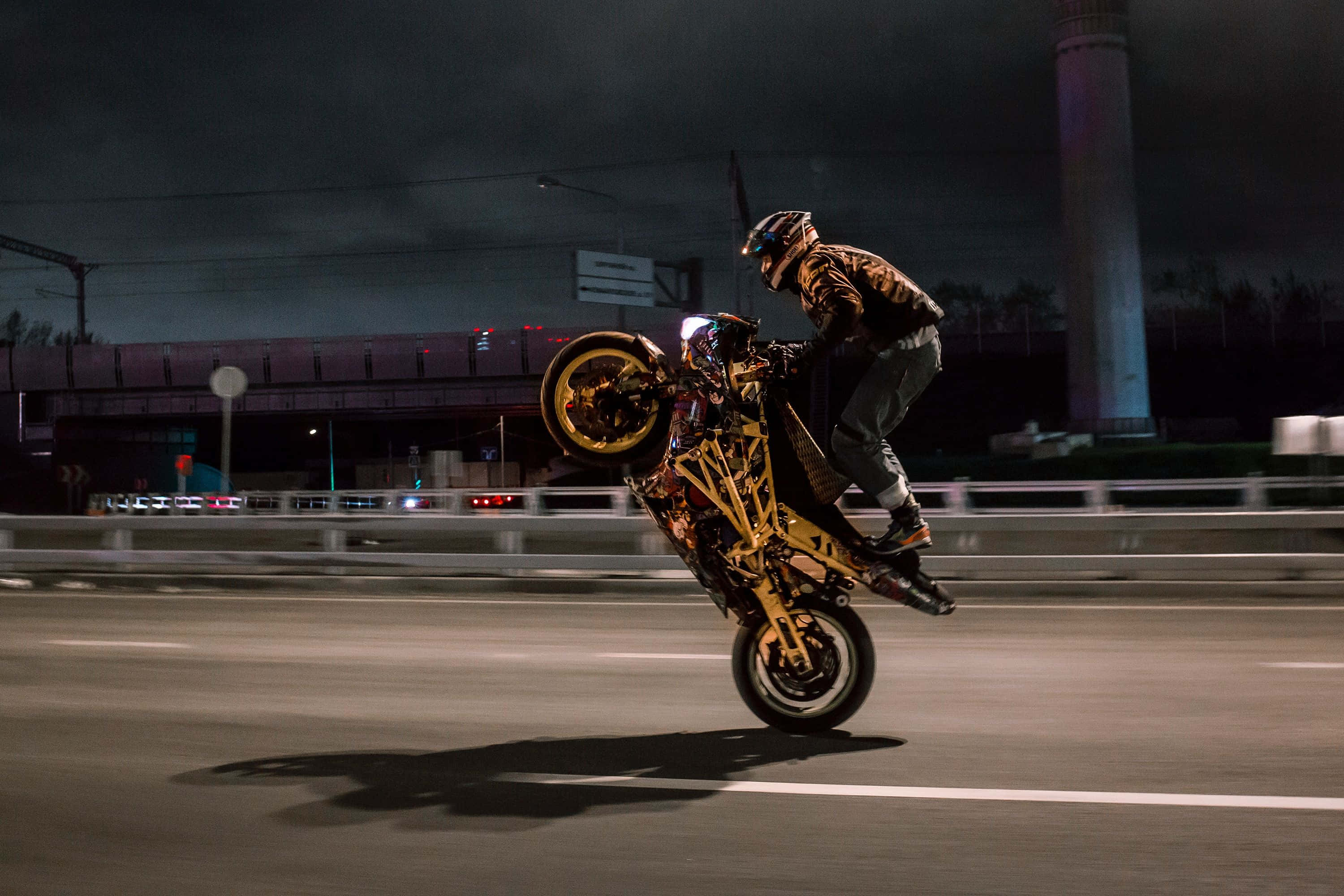 biker 桌布 壁紙 — 一名機車騎士在夜間於高速公路上，在人造燈光下，以黑暗天空為背景，做出大膽的翹前輪動作。