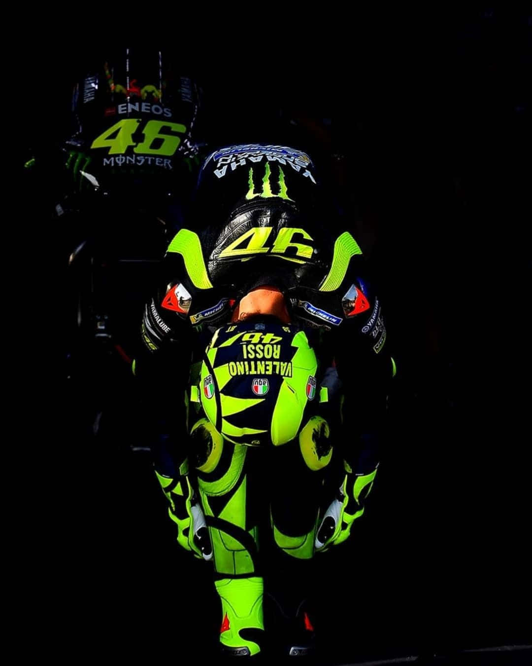 Valentino Rossi 桌布 壁紙 — 一名機車騎士身穿螢光綠和黑色賽車裝備，背上印有46號和「Valentino Rossi」，在黑暗背景前低伏著。