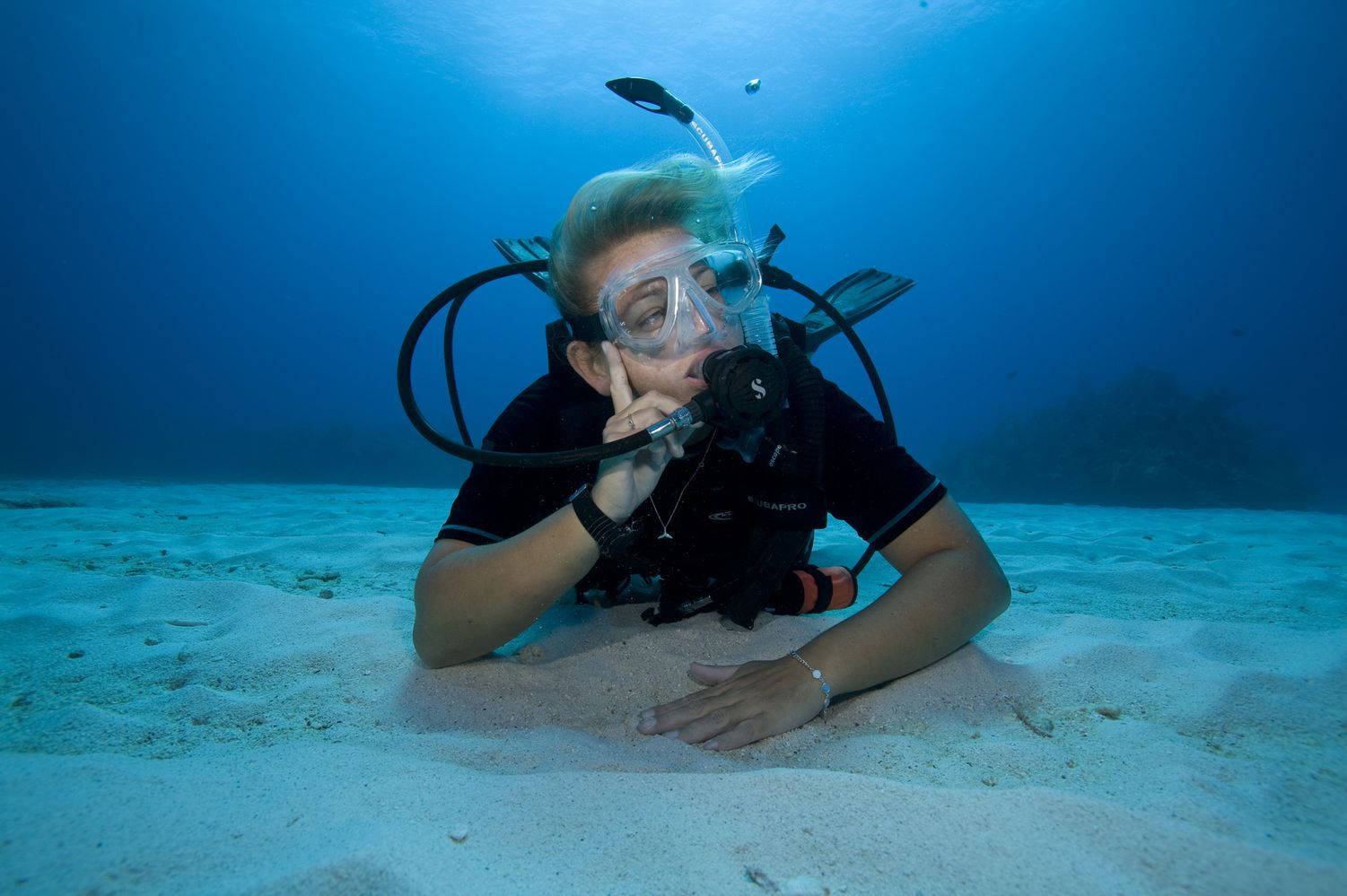 海洋 桌布 壁紙 — 一名水肺潛水員在沙質海床上休息，仰望清澈的藍色海水，陽光從上方過濾而下。