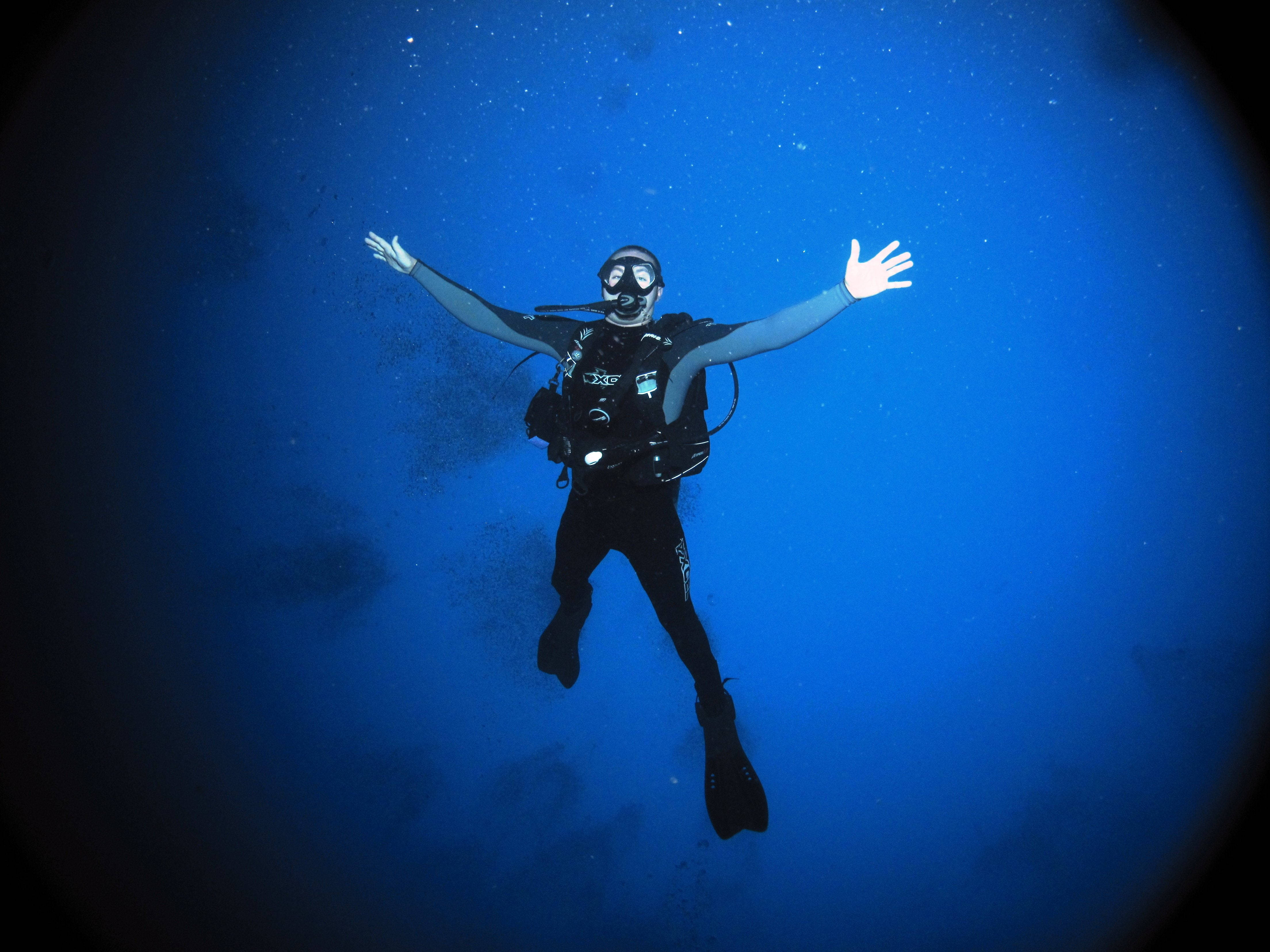 diving 桌布 壁紙 — 一名水肺潛水員在深藍色海水中伸展雙臂，被漂浮的粒子包圍，無重狀態下漂浮。