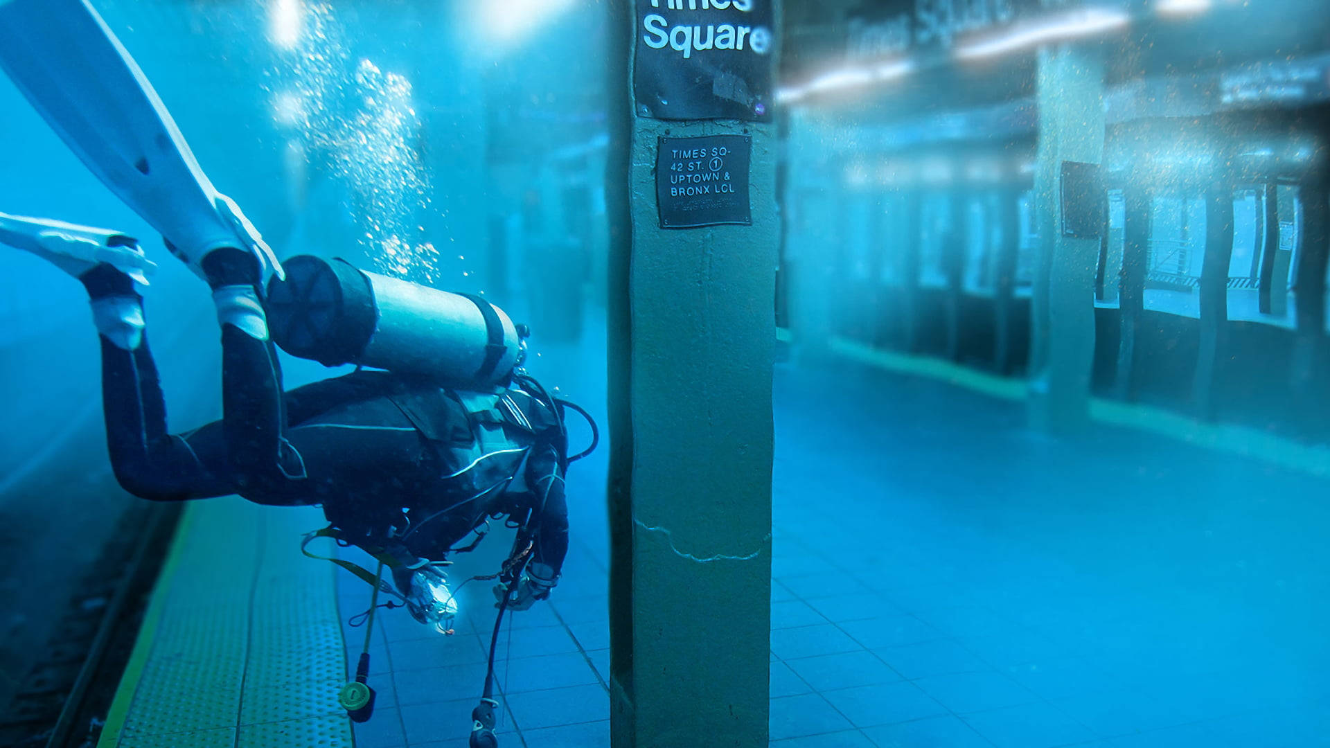 diving 桌布 壁紙 — 一名水肺潛水員探索一個水下地鐵站，'時代廣場'標誌在藍色薄霧中發光。
