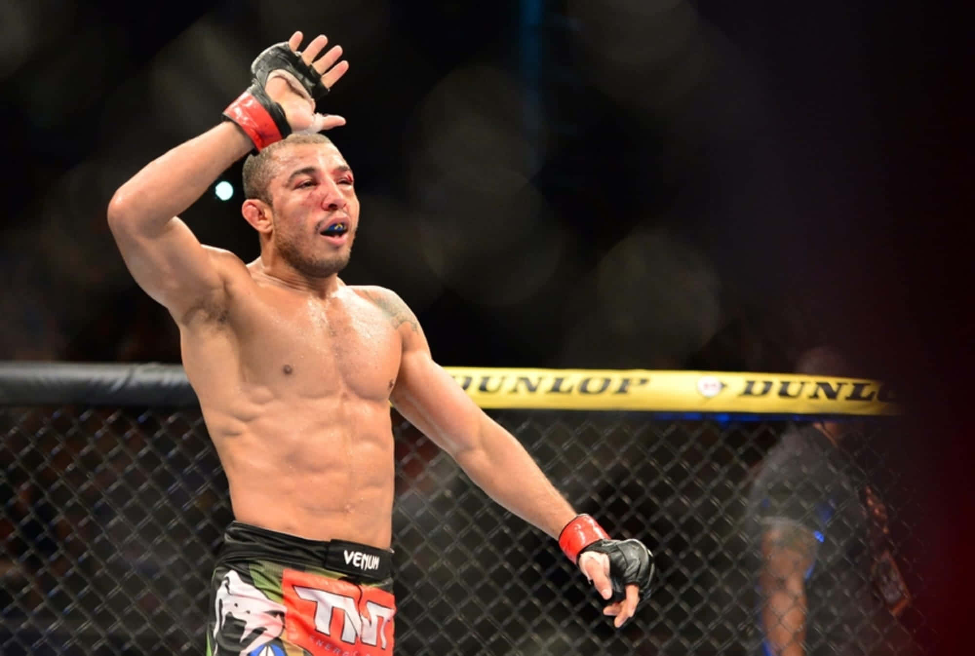UFC 桌布 壁紙 — 一名汗流浹背的MMA拳手在八角籠中高舉一隻手臂，張開嘴巴慶祝勝利。