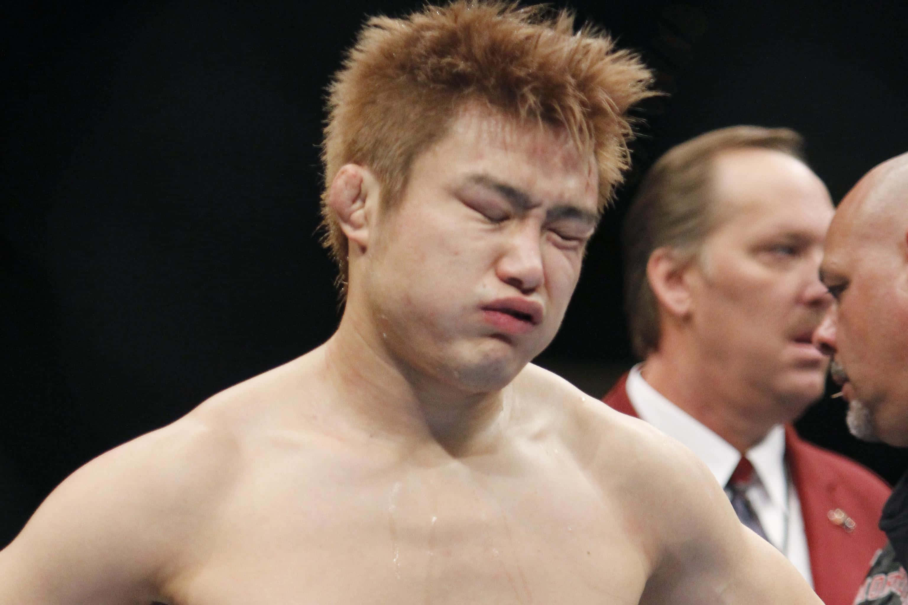 UFC 桌布 壁紙 — 一名汗流浹背的男性拳手在明亮的競技場燈光下，於搏擊運動比賽中因疲憊而扭曲表情。