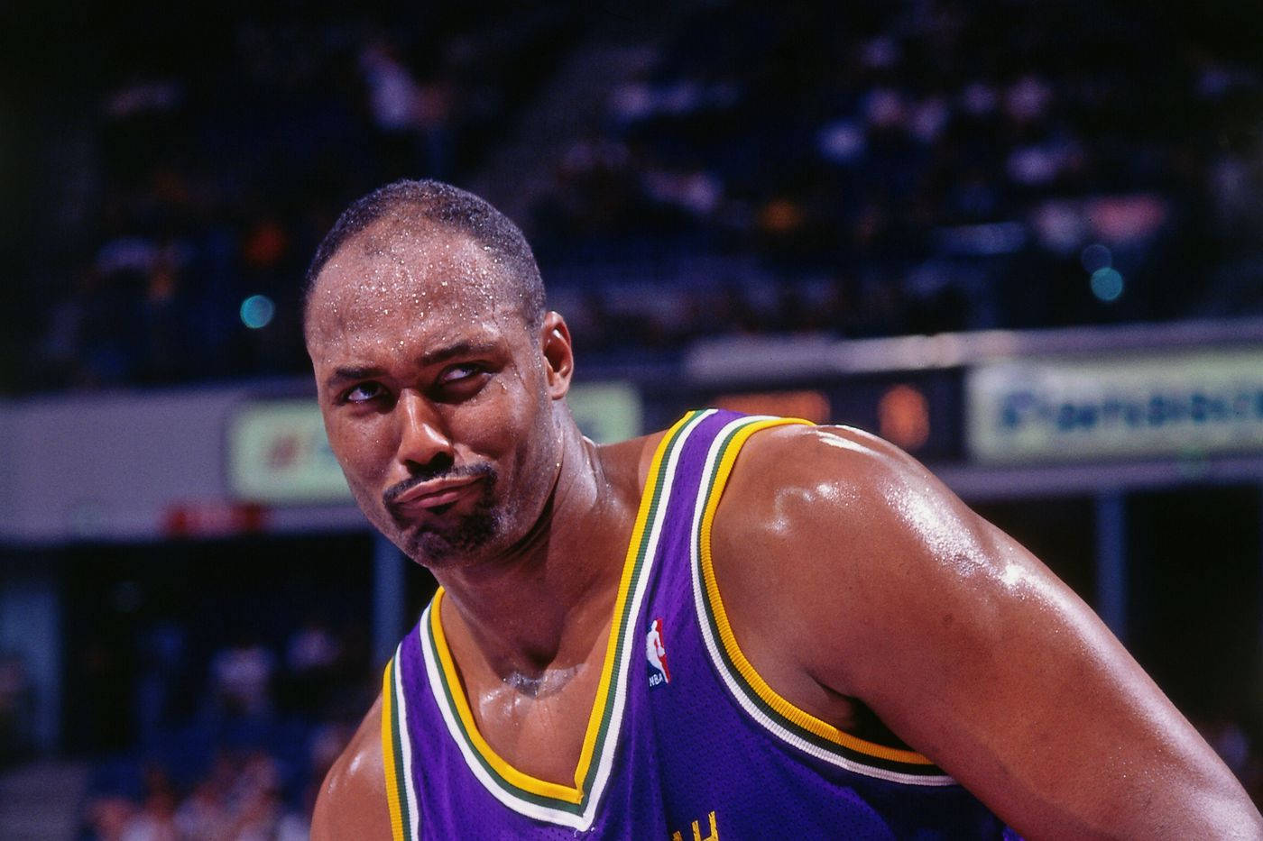 NBA 桌布 壁紙 — 一名汗流浹背的籃球運動員穿著紫色球衣，在場館燈光下比賽中專注地凝視。