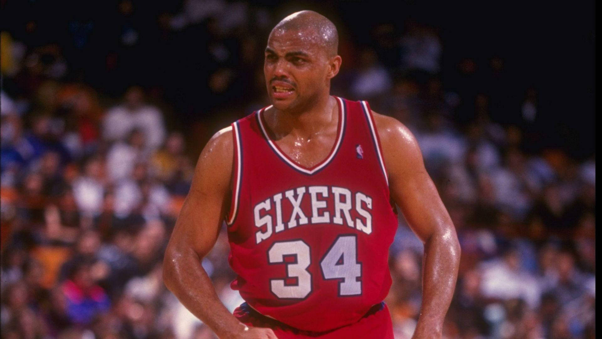 NBA 桌布 壁紙 — 一名汗流浹背的籃球運動員身穿紅色Sixers 34號球衣，在場館燈光下於比賽中凝視前方。