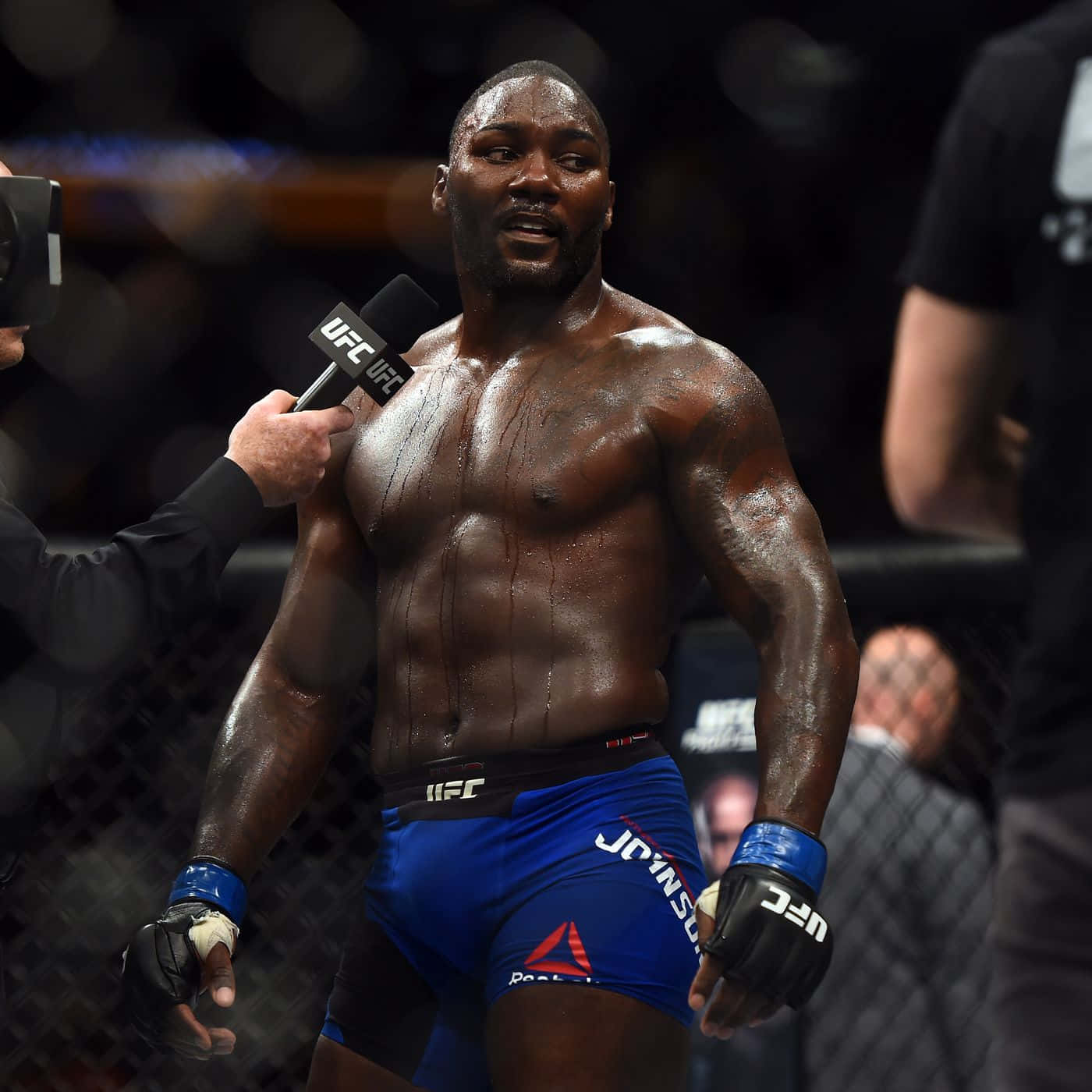 MMA 桌布 壁紙 — 一名汗流浹背的肌肉發達拳手穿著藍色短褲，站在UFC八角籠內接受賽後訪問。