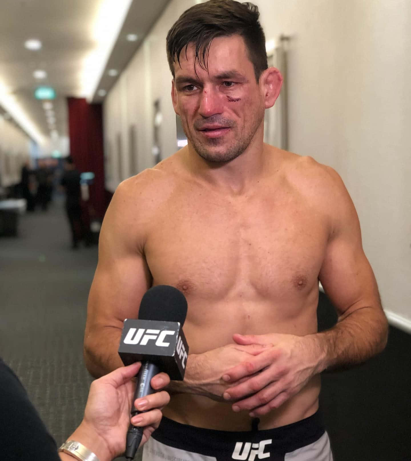 Champion 桌布 壁紙 — 一名沒穿上衣的UFC拳手，臉上帶有瘀傷和流血的眼睛，站在走廊裡握著麥克風，在比賽之後。