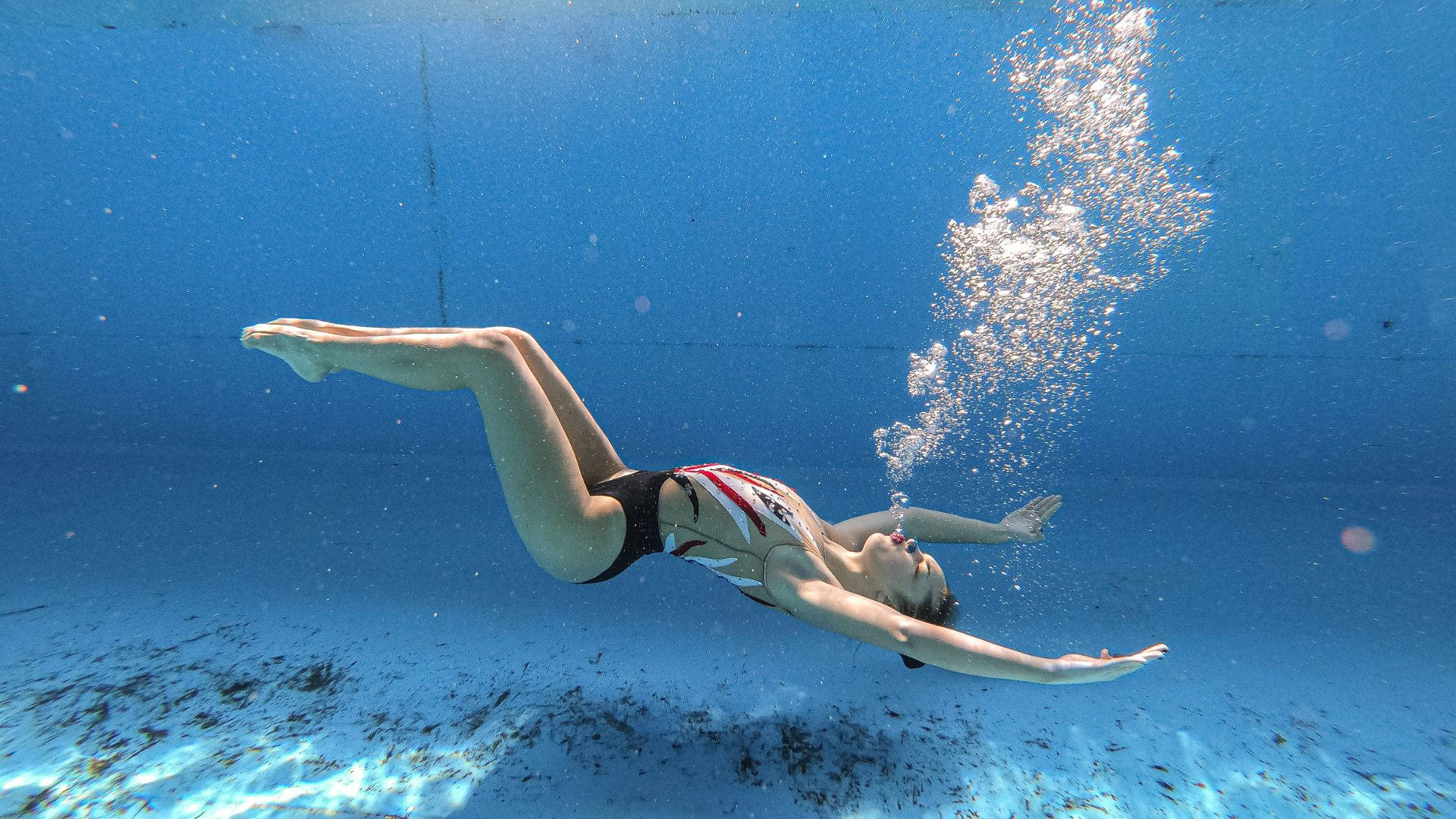 Swimming 桌布 壁紙 — 一名泳者在泳池中優雅地在水下滑行，身後留下一串氣泡。