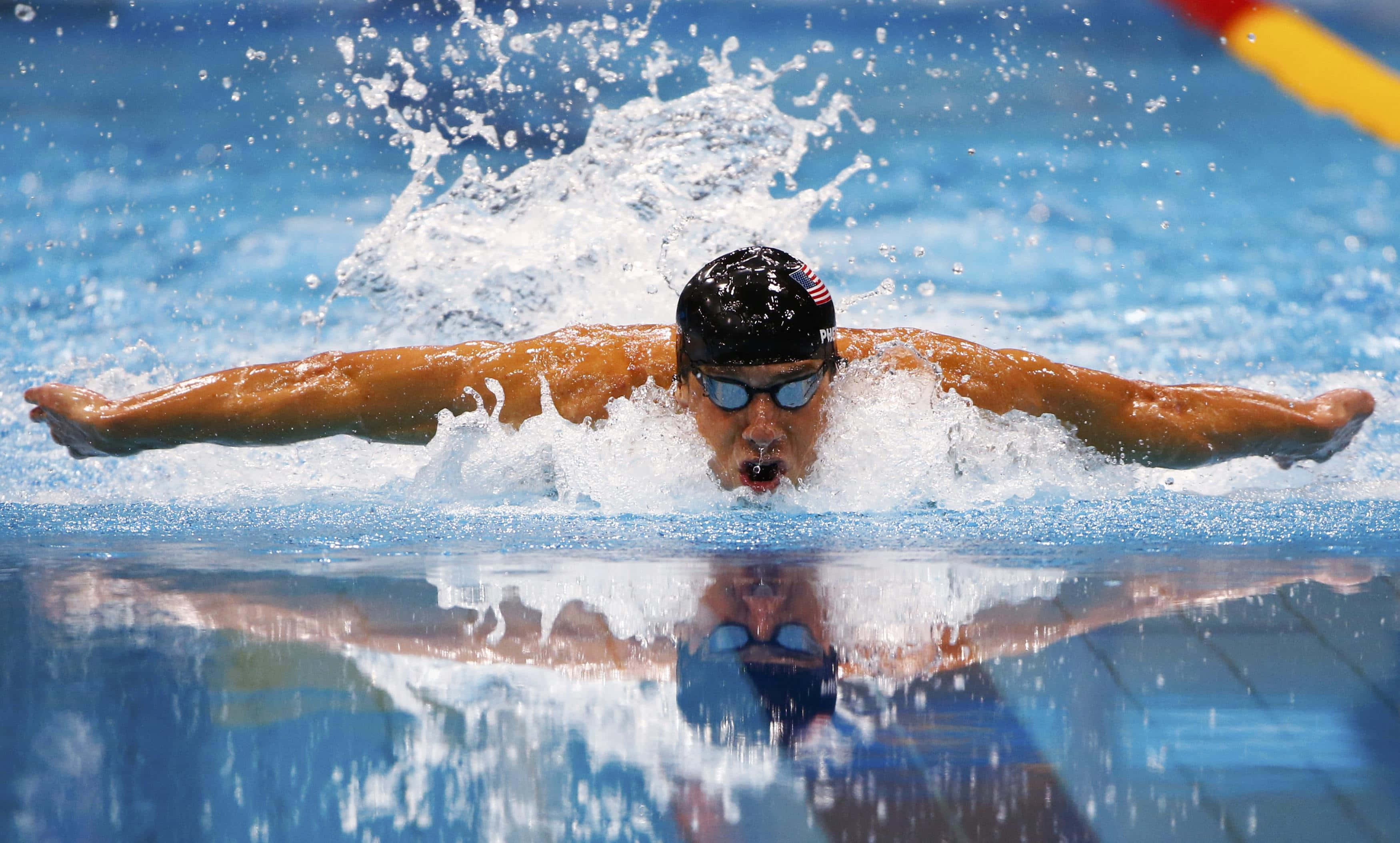 Swimming 桌布 壁紙 — 一名泳者在競賽泳池中執行強勁的蝶式，雙臂大張，水花四濺。