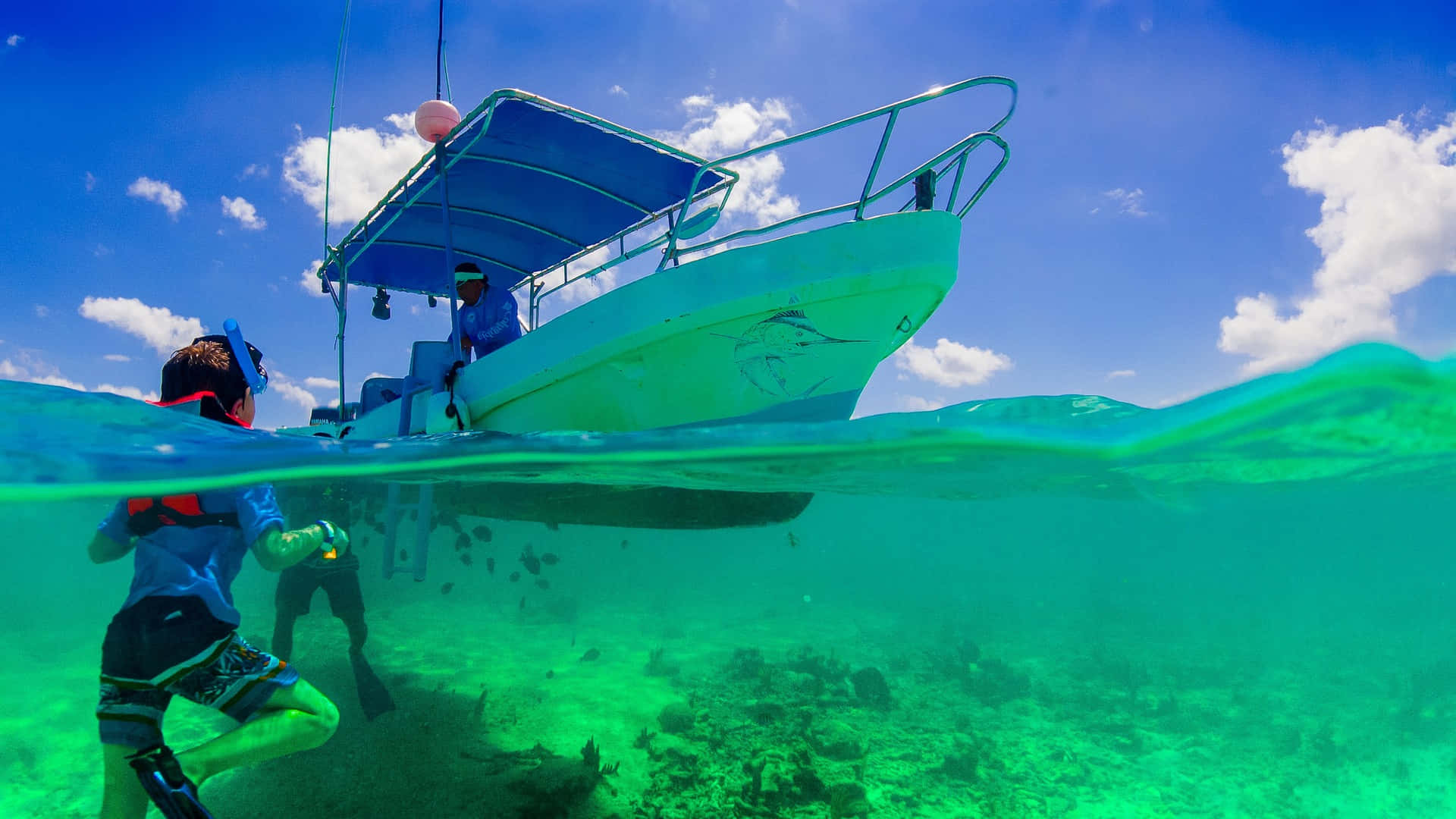 Cancun 桌布 壁紙 — 一名浮潛者在明亮的藍天白雲下，探索綠松色船隻下方的 vibrant 珊瑚礁。