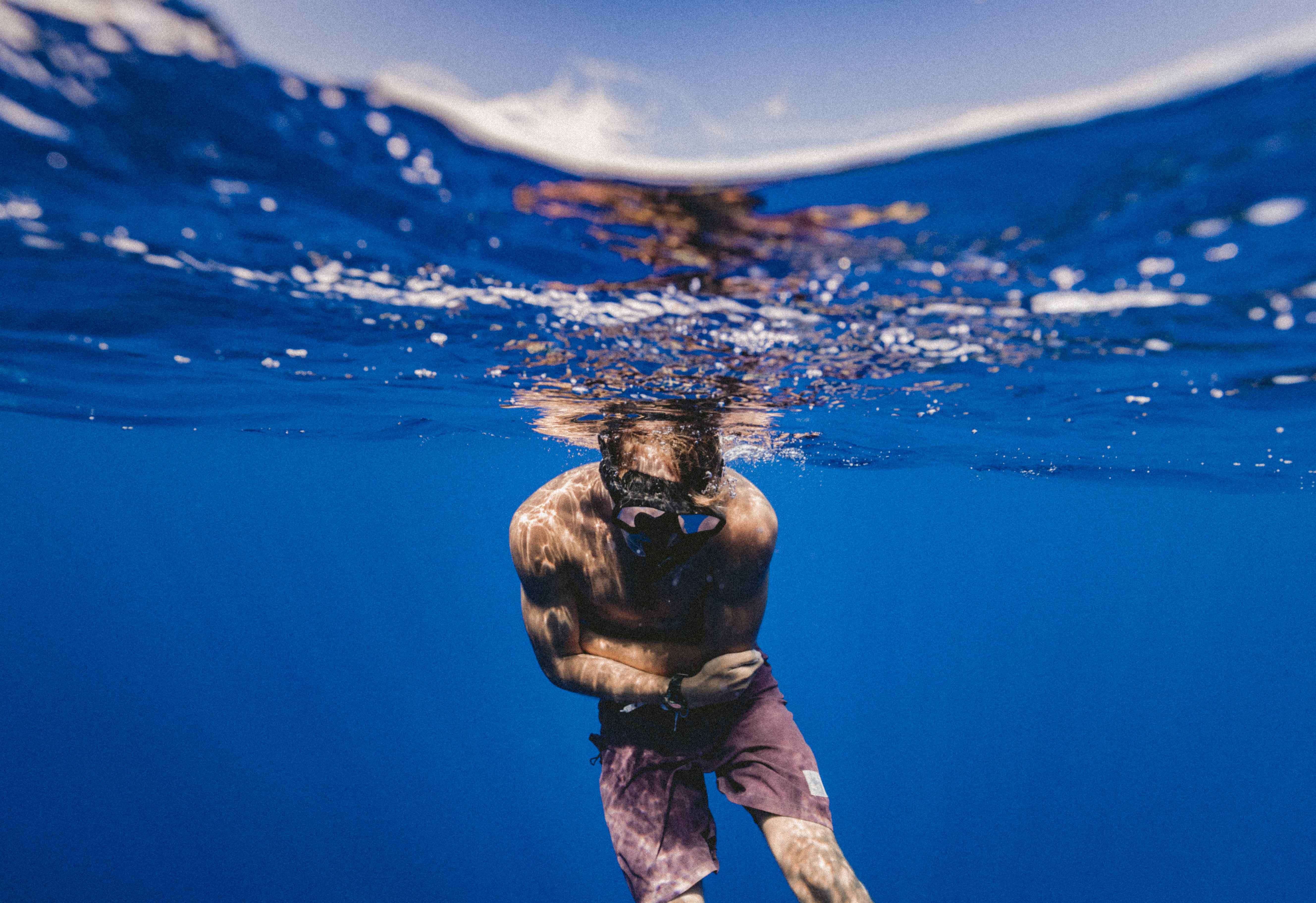 Snorkeling 桌布 壁紙 — 一名浮潛者在水晶般清澈的藍色海洋中於水下滑行，陽光從上方水面過濾而下。