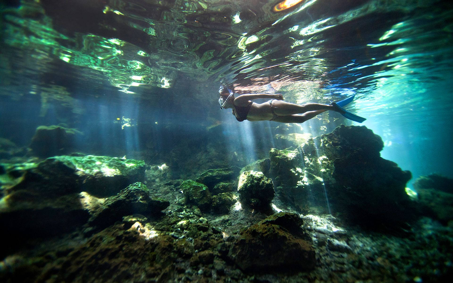 Snorkeling 桌布 壁紙 — 一名浮潛者在陽光普照的碧綠海水中，於岩石海底上方優雅地滑行。