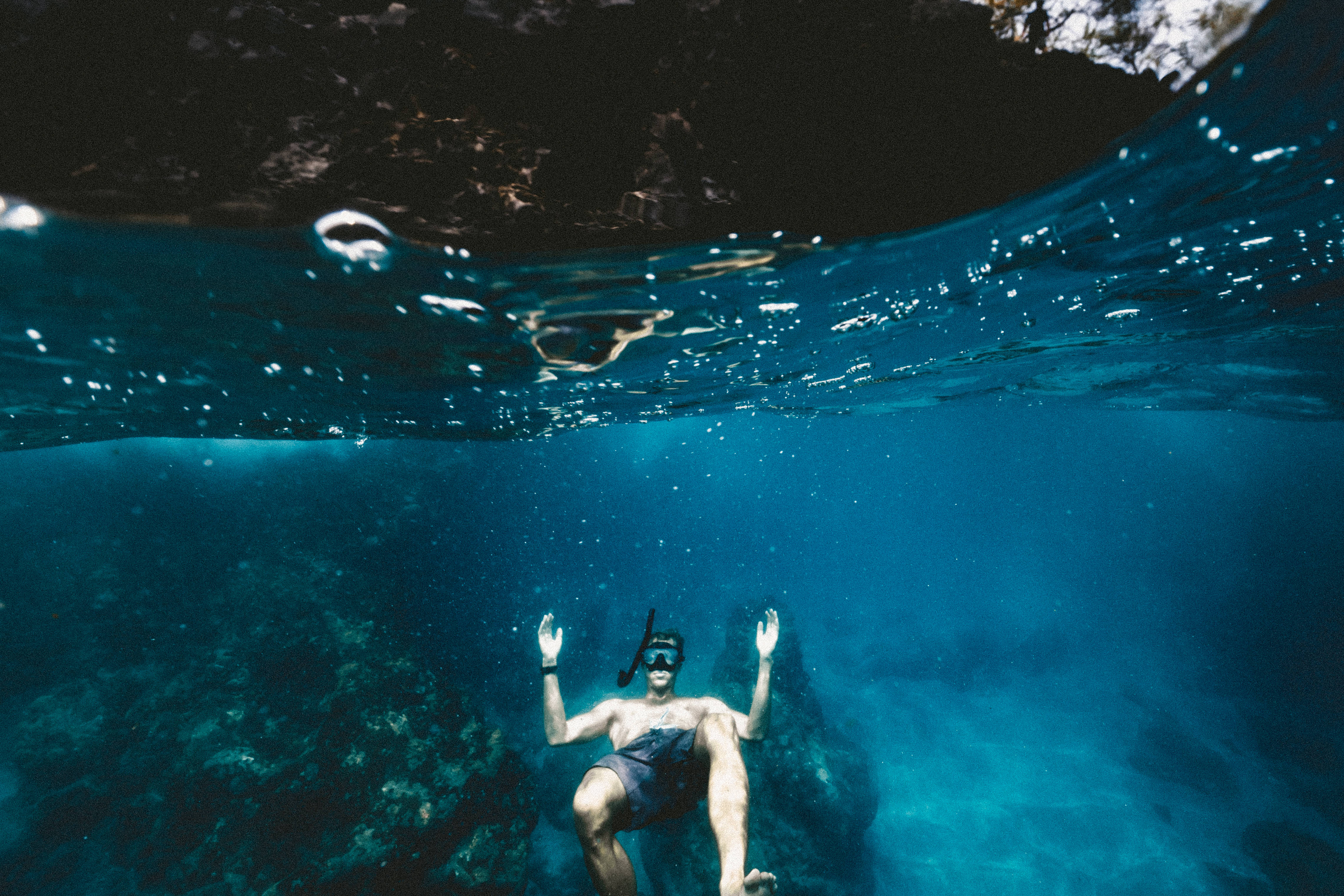 Snorkeling 桌布 壁紙 — 一名浮潛者在陽光照射的水面下平靜地漂浮，雙臂舉起，在清澈的碧綠海水中充滿驚奇。