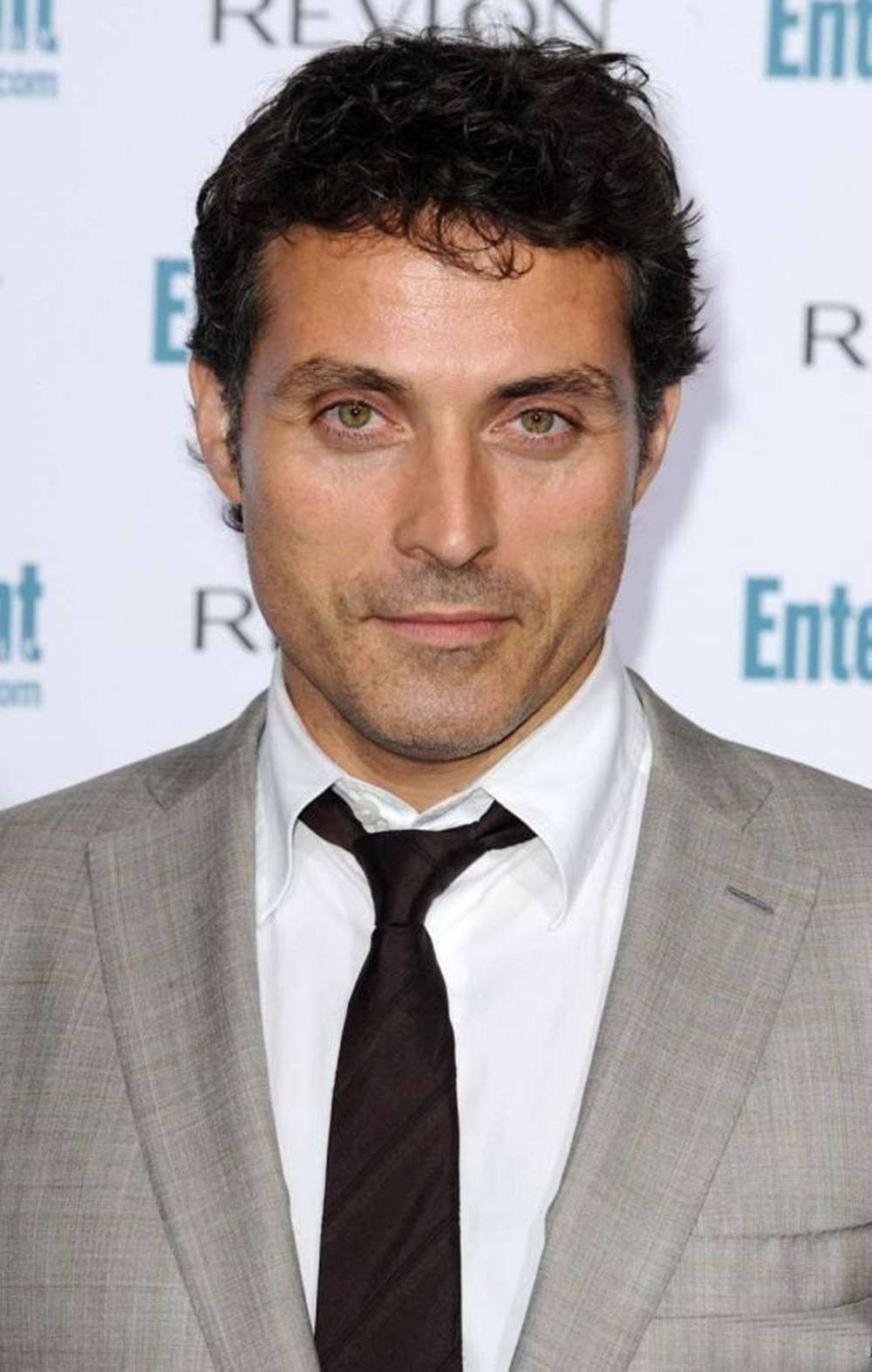 actor 桌布 壁紙 — 一名深色捲髮、綠眼睛的男子在記者會上穿著灰色西裝、白襯衫和深色領帶。
