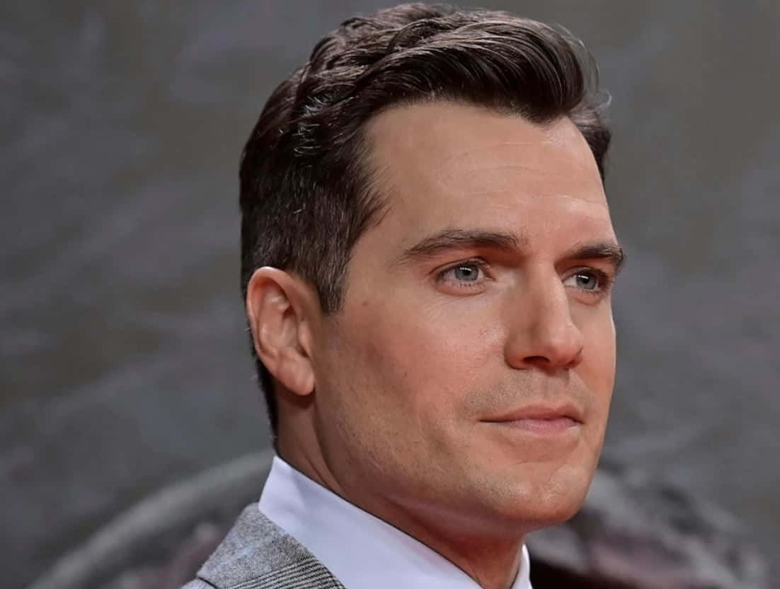 Henry Cavill 桌布 壁紙 — 一名深色造型頭髮、藍眼睛男士的特寫肖像，身穿灰色西裝和白色襯衫。