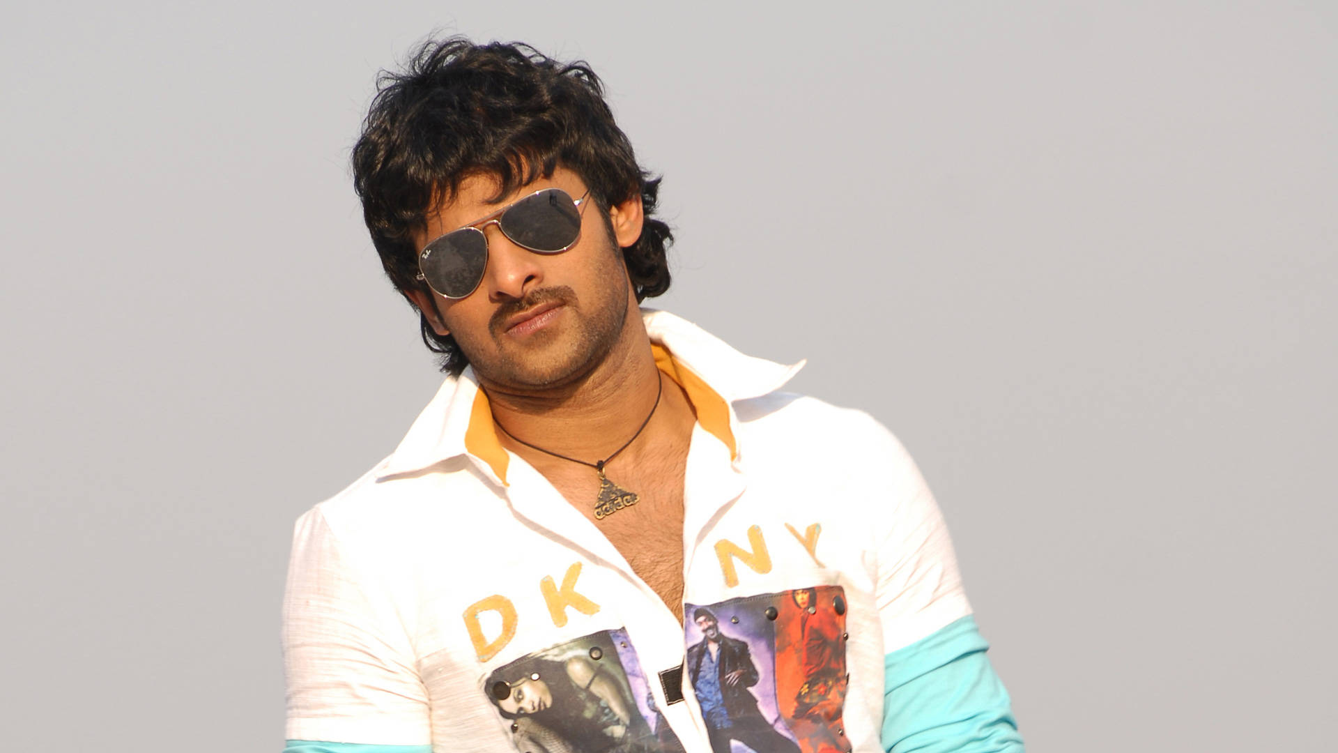 Prabhas HD 桌布 壁紙 — 一名深色頭髮、戴太陽眼鏡的男子，在純灰色背景前穿著白色圖案T恤。