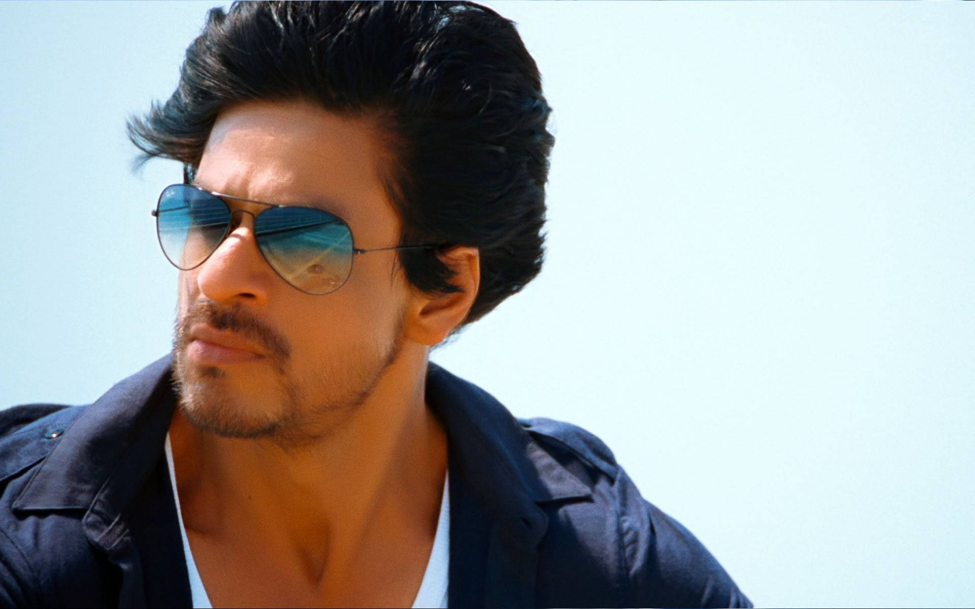 Shah Rukh Khan 桌布 壁紙 — 一名深色頭髮、戴著太陽眼鏡的男子，在明亮的藍天下若有所思地凝視著。