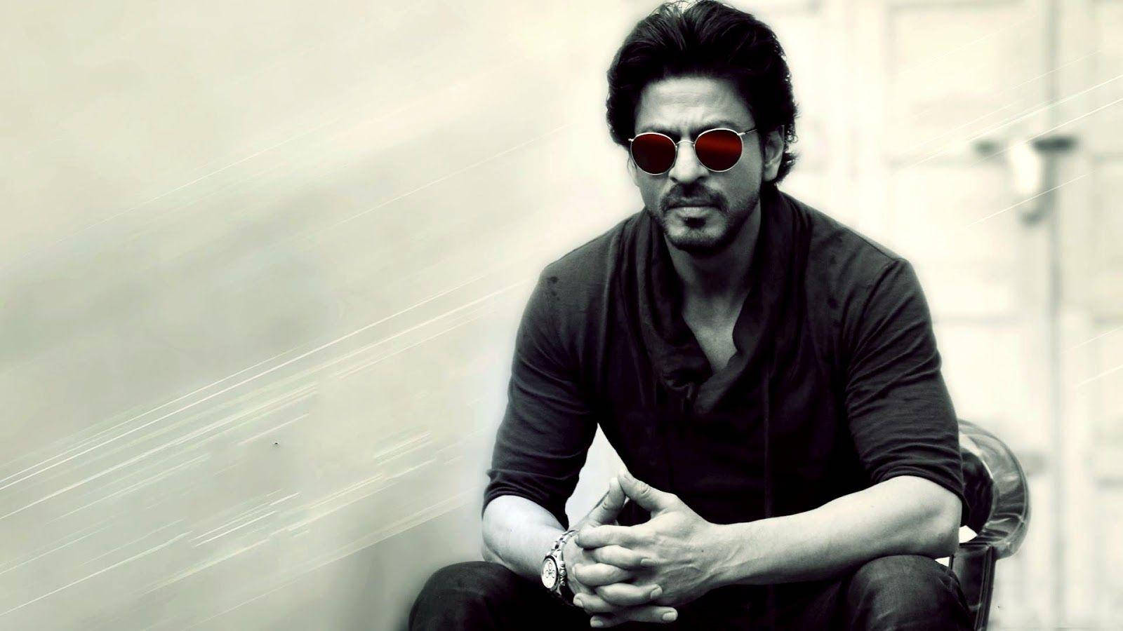 Shahrukh 桌布 壁紙 — 一名深色頭髮、戴著紅色太陽眼鏡的男子自信地坐在椅子上，背景模糊，帶有光線條紋。
