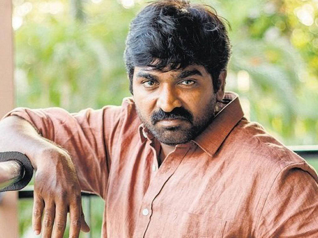 vijay HD 桌布 壁紙 — 一名深色頭髮、留鬍鬚的男子身穿鏽色襯衫，靠在欄杆上，背景是模糊的綠色樹葉。