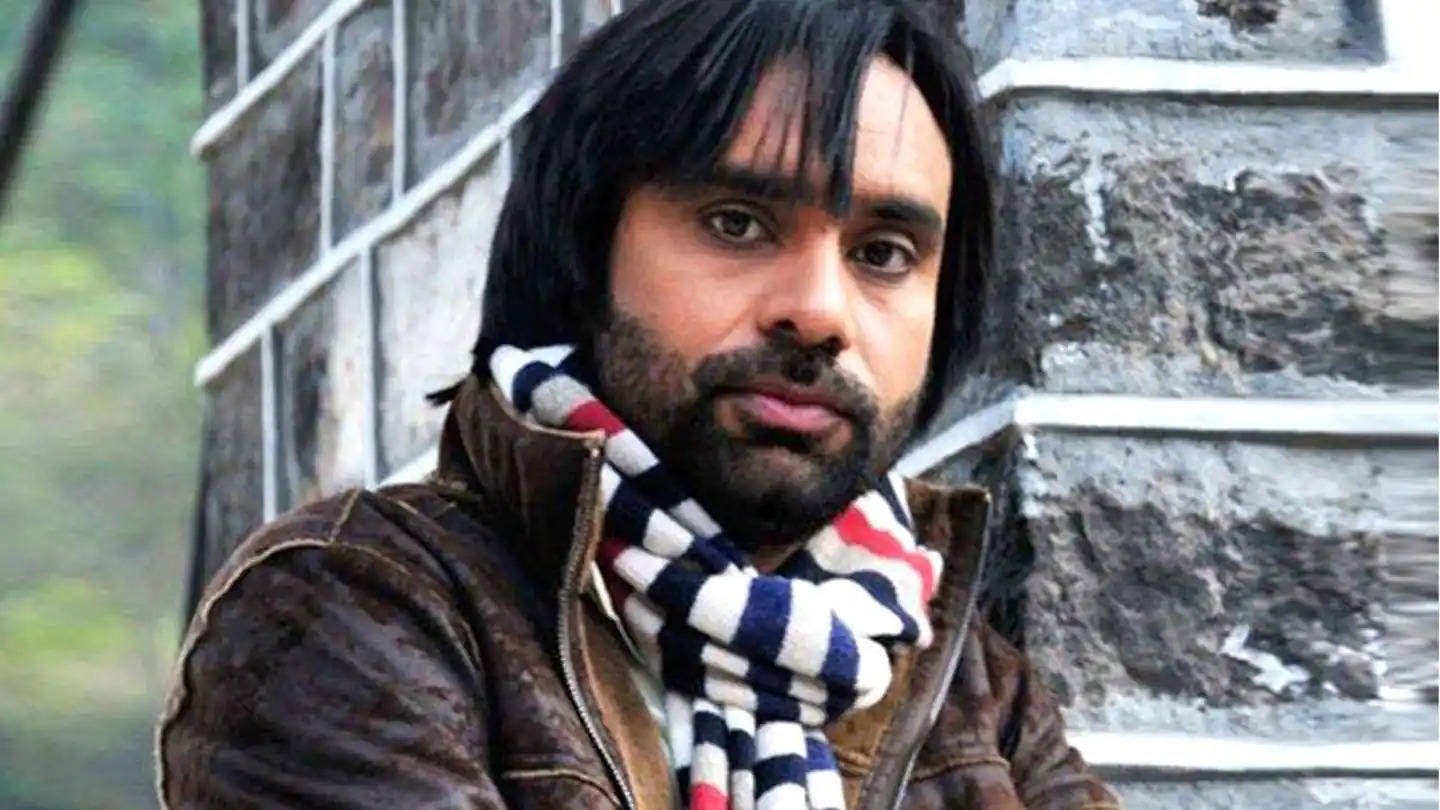Indian 桌布 壁紙 — 一名深色頭髮和鬍鬚的男子，在石牆背景下戴著條紋圍巾和棕色外套。