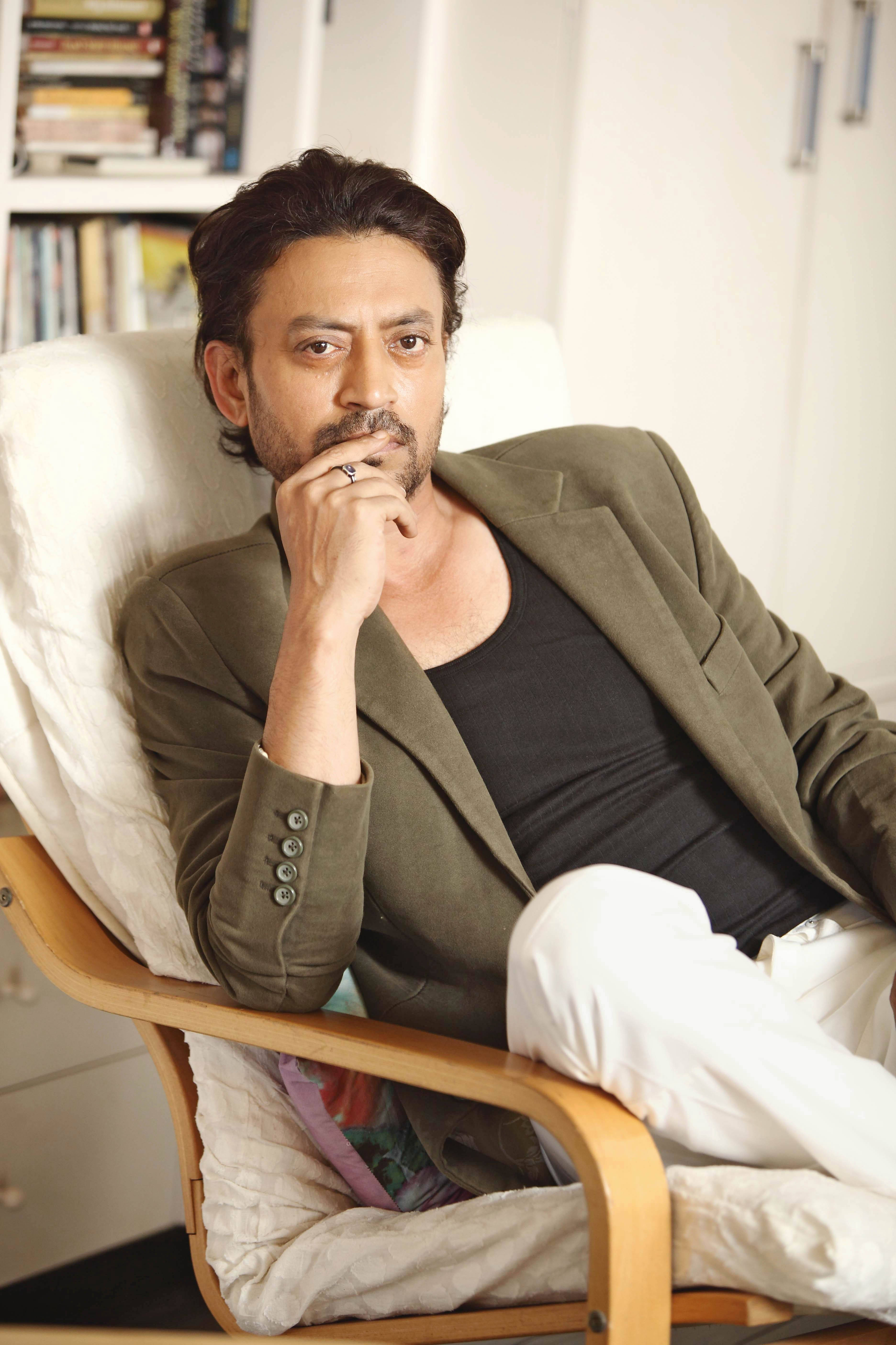 Irrfan Khan 桌布 壁紙 — 一名深色頭髮和鬍鬚的男子，穿著綠色西裝外套和白色長褲，若有所思地坐在室內的木椅上。