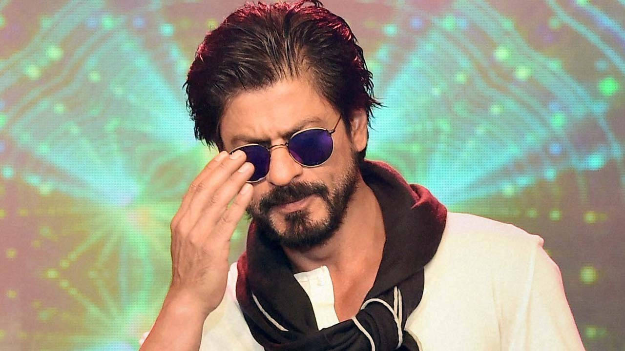 Shahrukh 桌布 壁紙 — 一名深色頭髮和鬍鬚的男子在發光的抽象背景前調整他的圓形紫色太陽眼鏡。