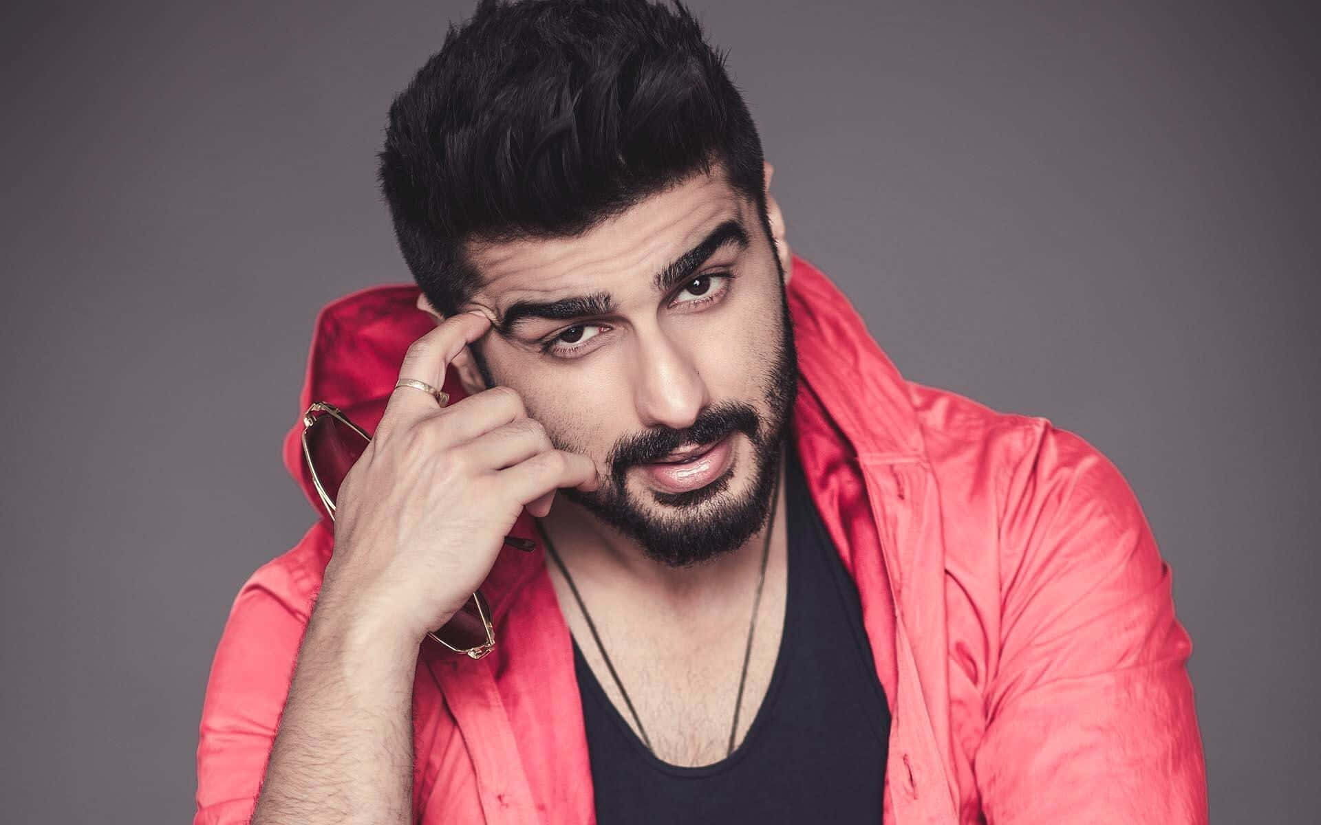 Arjun Kapoor 桌布 壁紙 — 一名深色頭髮和鬍鬚的男子穿著紅色外套，在灰色背景前將眼鏡靠近臉部。