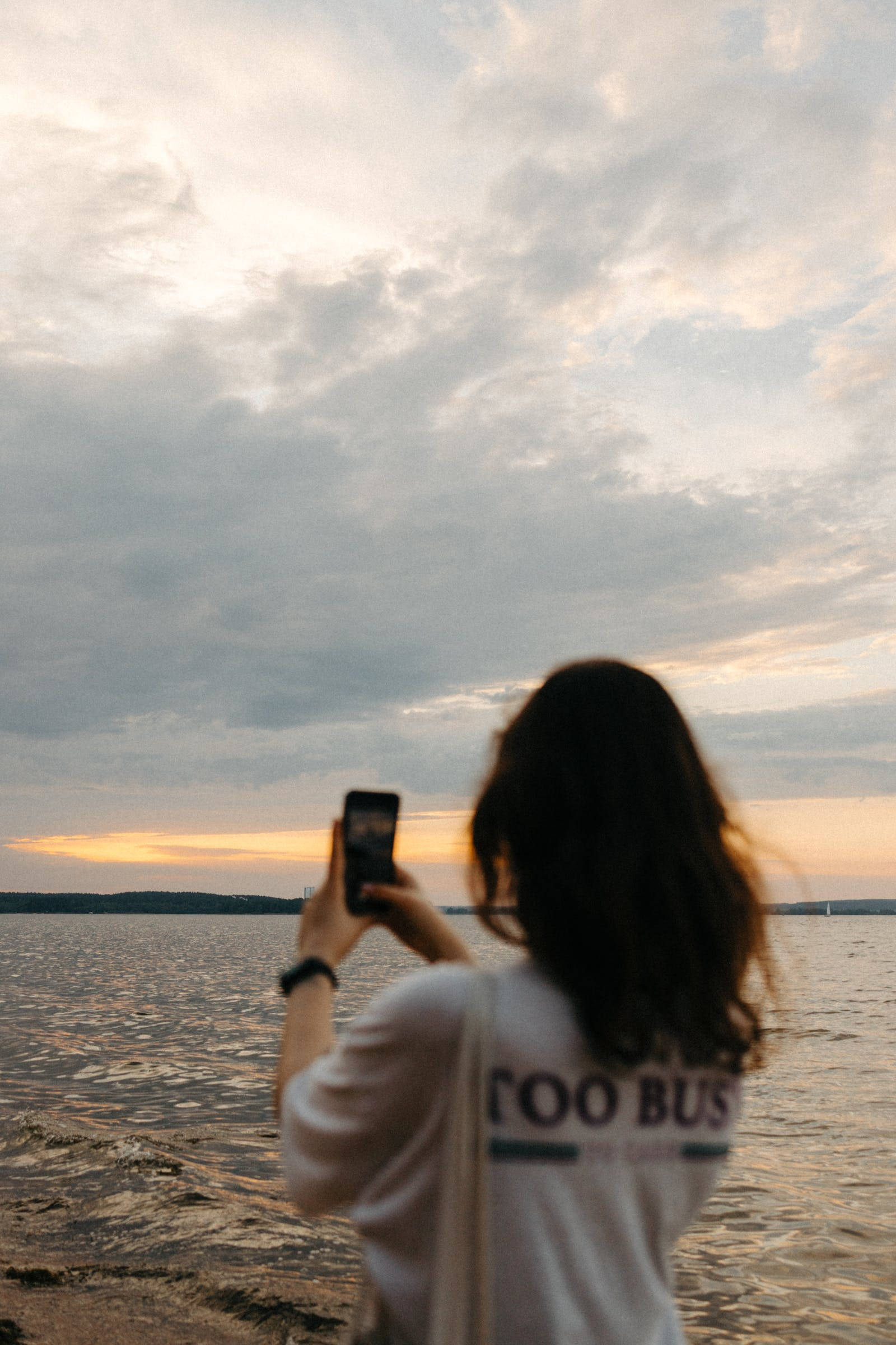 Nature iPhone 桌布 壁紙 — 一名深色頭髮的人在海濱拍攝日落，天空多雲。