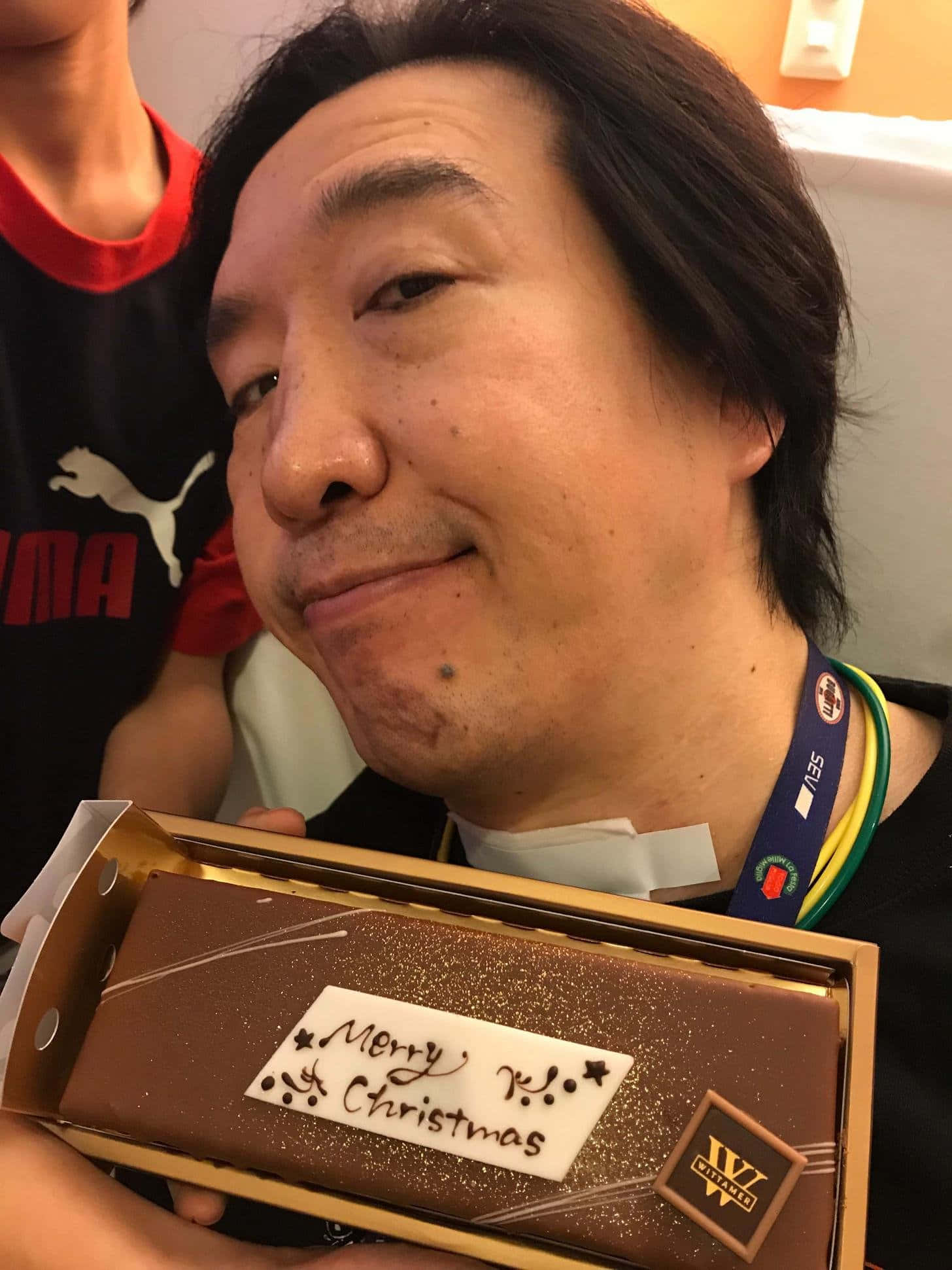 蛋糕 桌布 壁紙 — 一名深色頭髮的男子微笑著，手持一個金色盒子，裡面裝著標有「Merry Xmas」的巧克力棒。