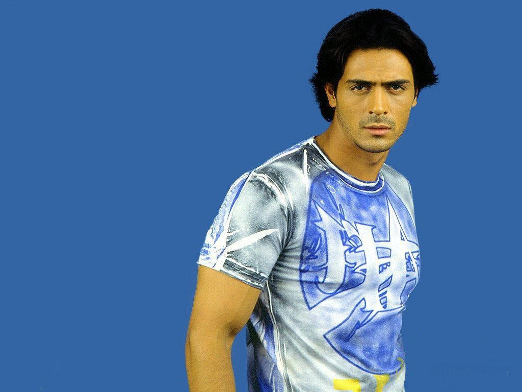 Arjun Rampal 桌布 壁紙 — 一名深色頭髮的男子穿著藍色和銀色圖案T恤，背景為純藍色。