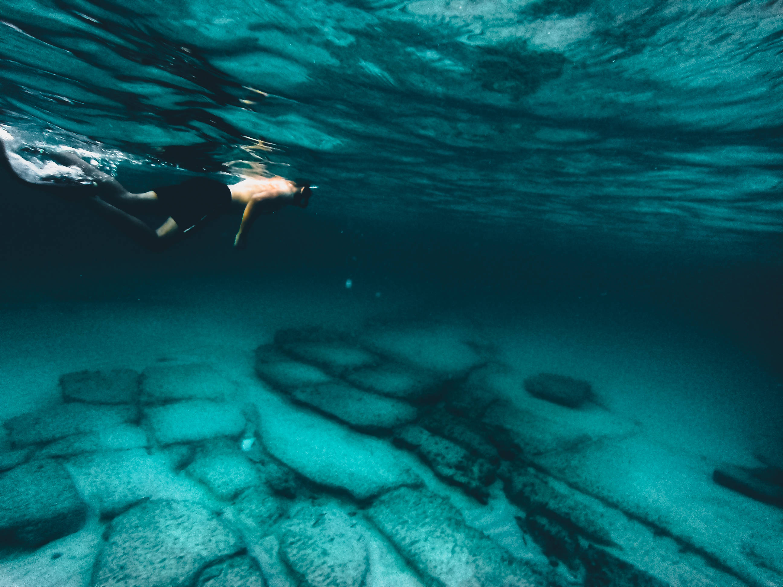 Snorkeling 桌布 壁紙 — 一名游泳者滑過清澈的碧綠海水，在陽光照耀的岩石海底上方。