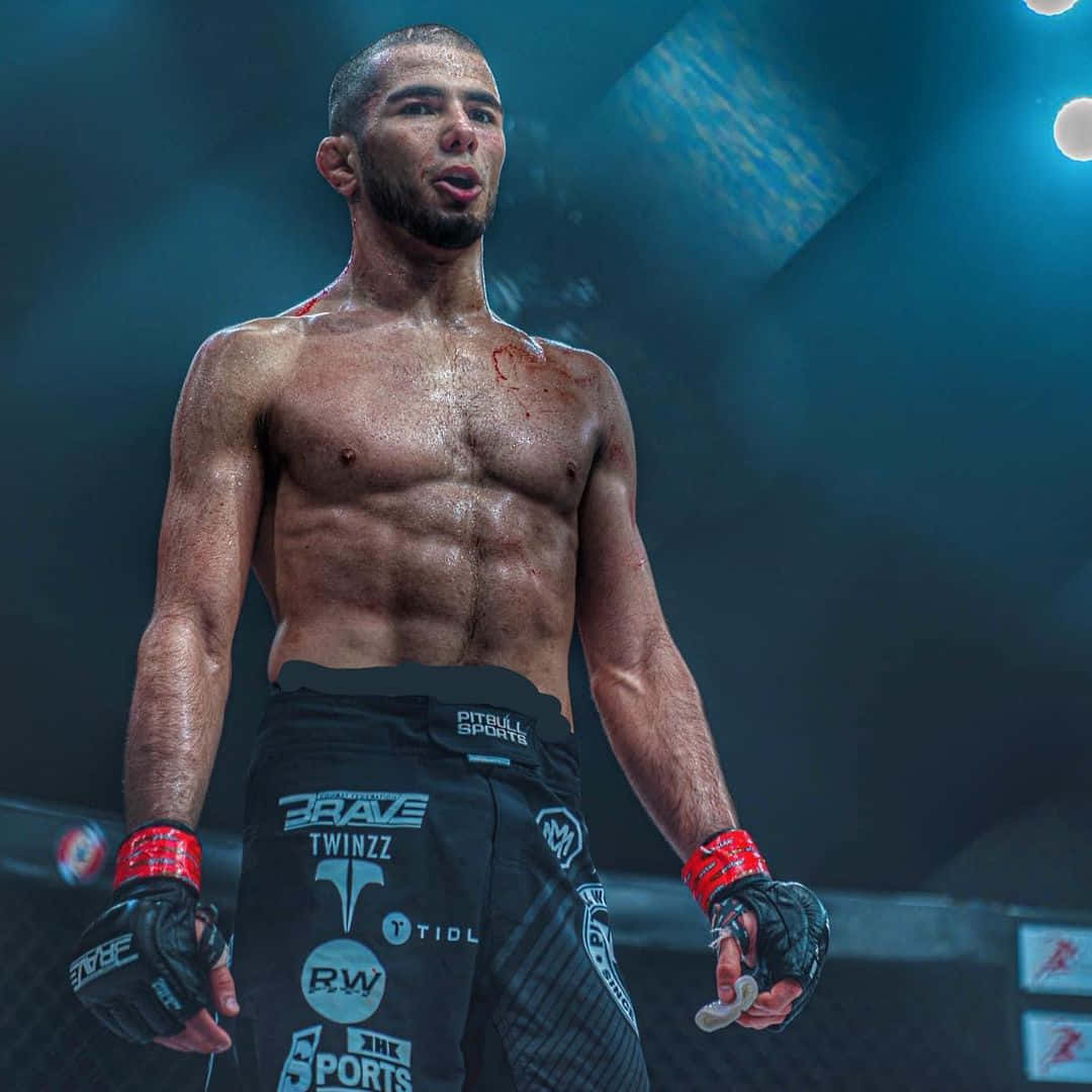 MMA 桌布 壁紙 — 一名渾身是血、筋疲力盡的混合武術選手在戲劇性的藍色燈光下，於八角籠中經歷了一場殘酷的戰鬥後站立著。